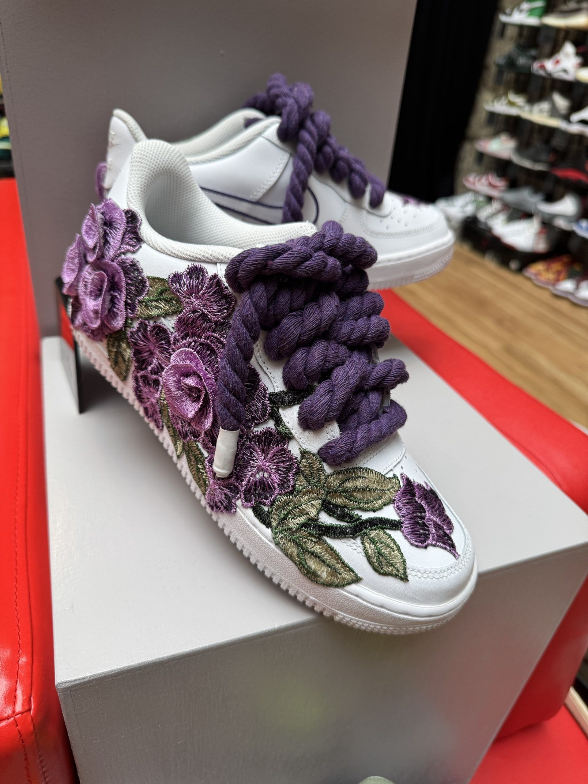 White sneakers with purple floral embroidery and thick purple laces.