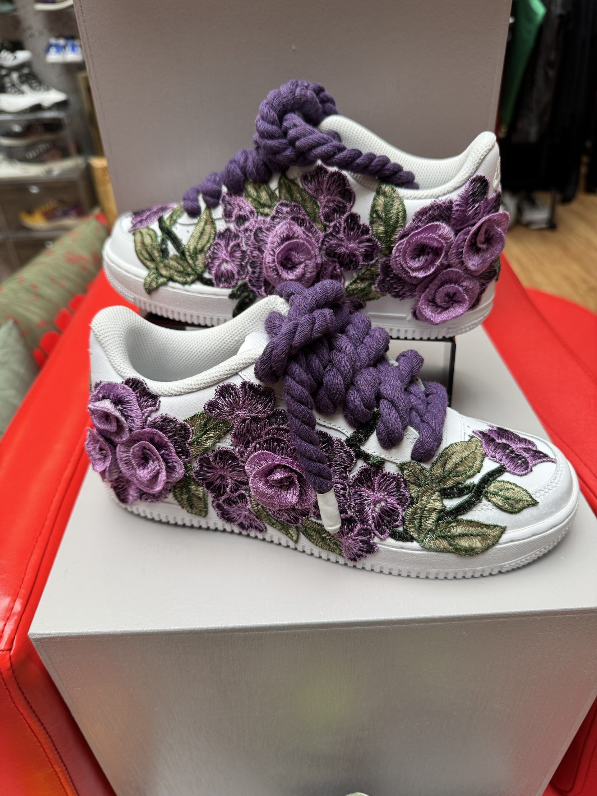 White sneakers with purple floral embroidery and thick purple laces.