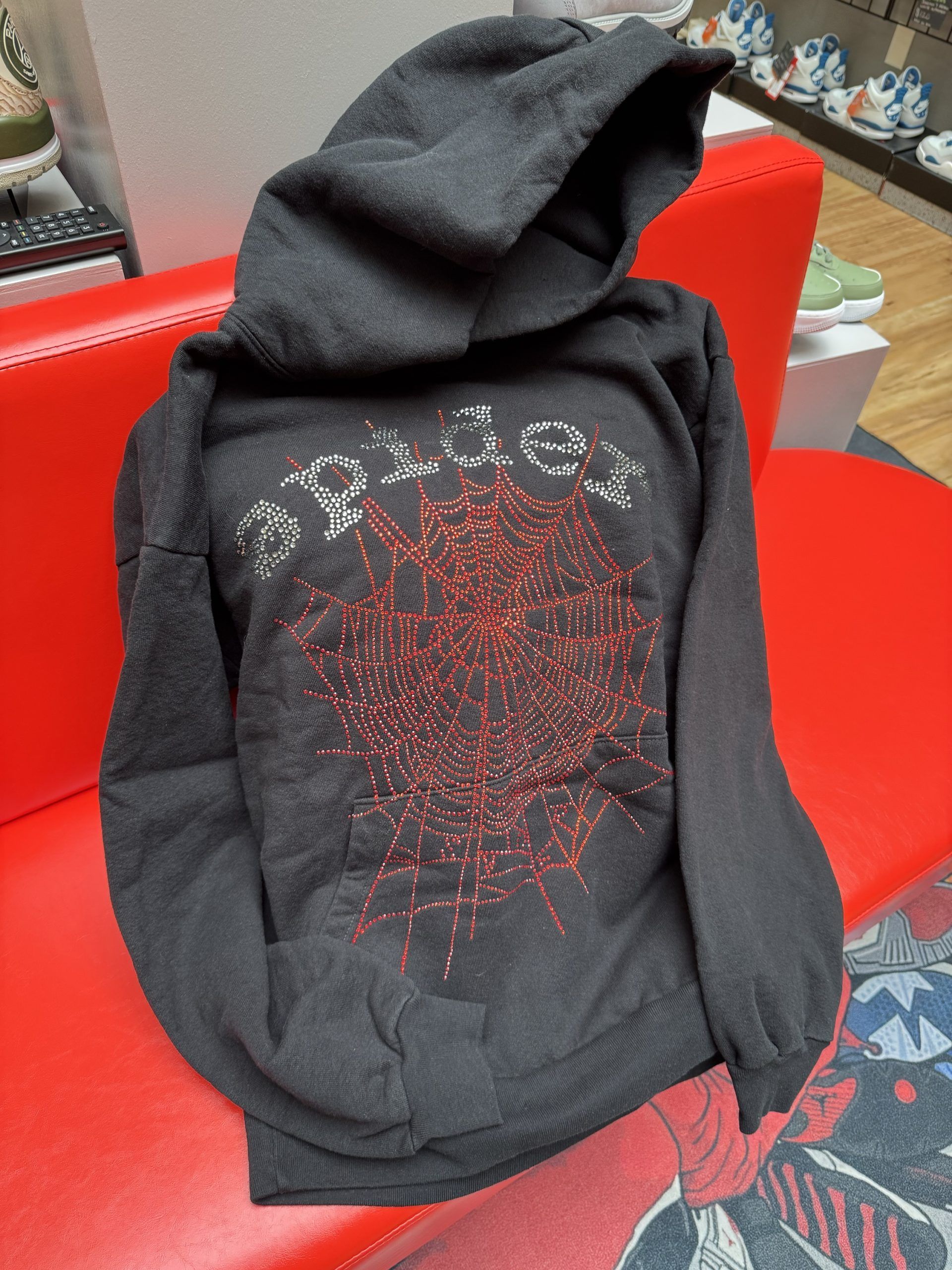 Black hoodie with red sparkly design on red couch in store.