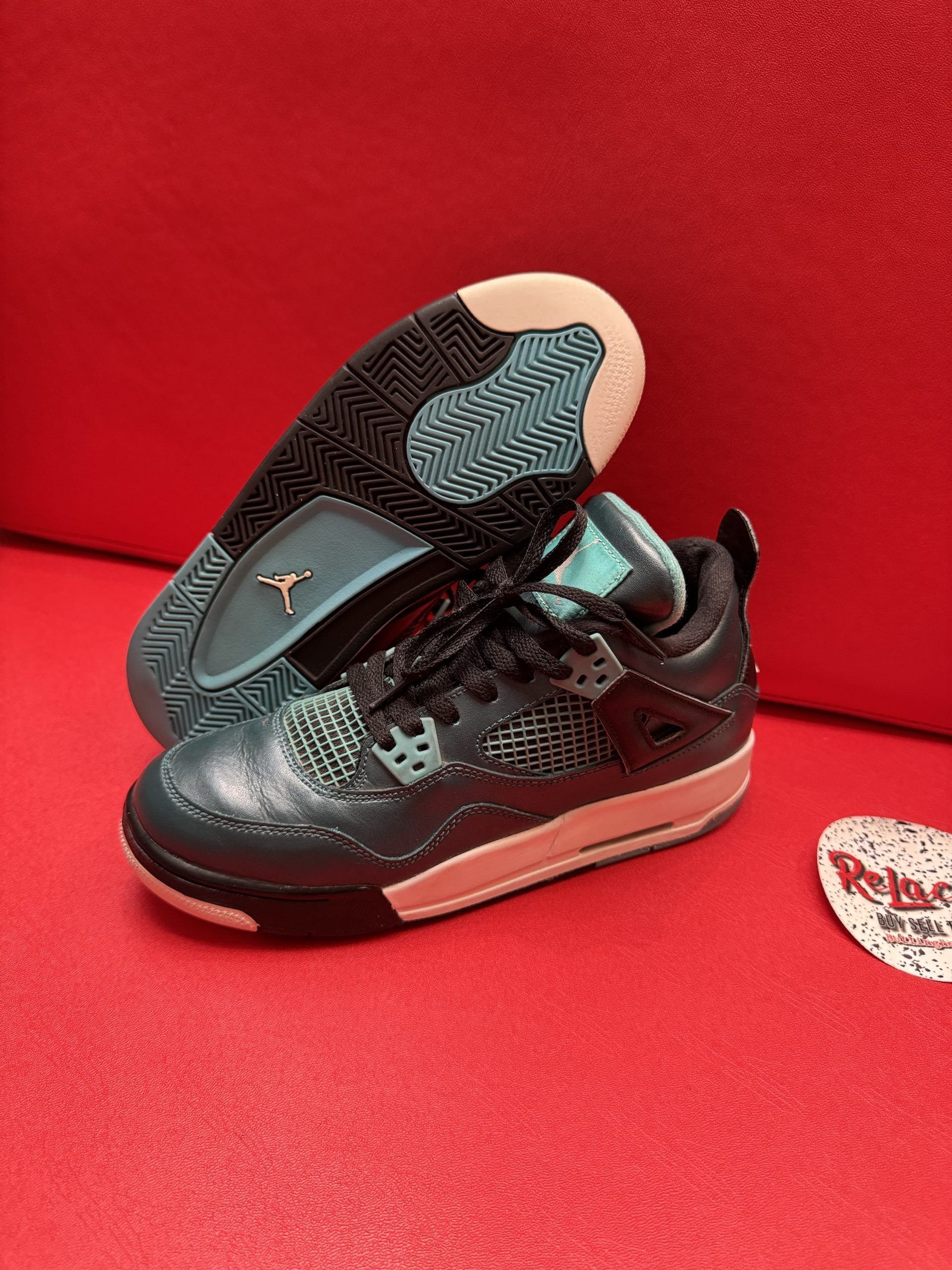A teal and black Air Jordan sneaker with a white sole against a red background.