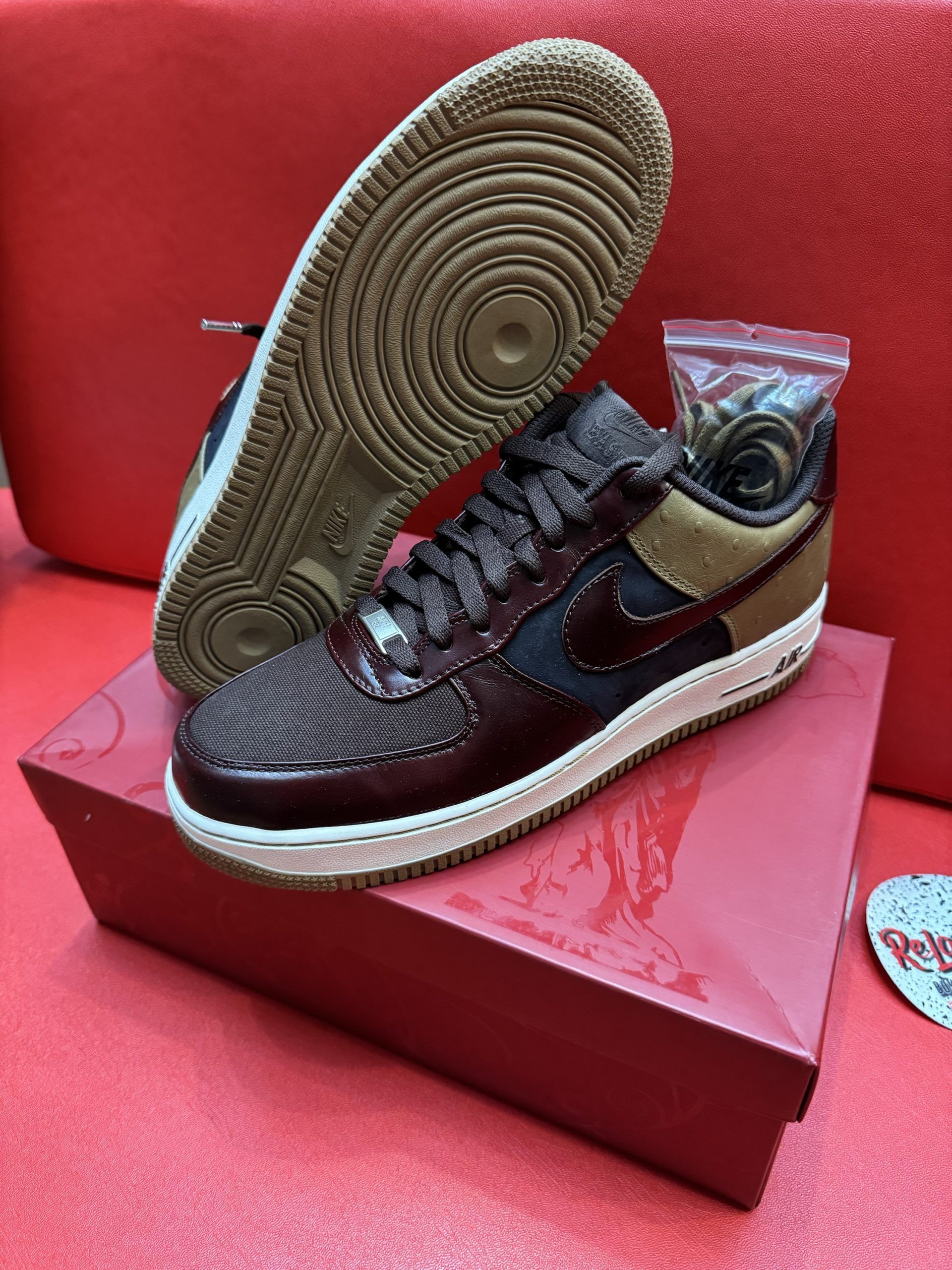 Air Force 1 sneakers on a red box, featuring brown, navy, and tan colors with a gum sole and extra laces.