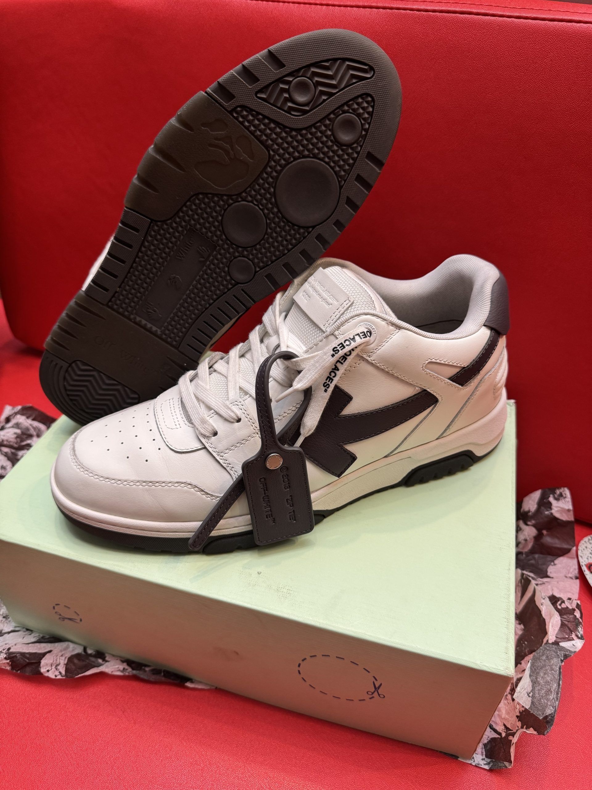 White and black sneaker with brown sole on a light green box, on a red surface.