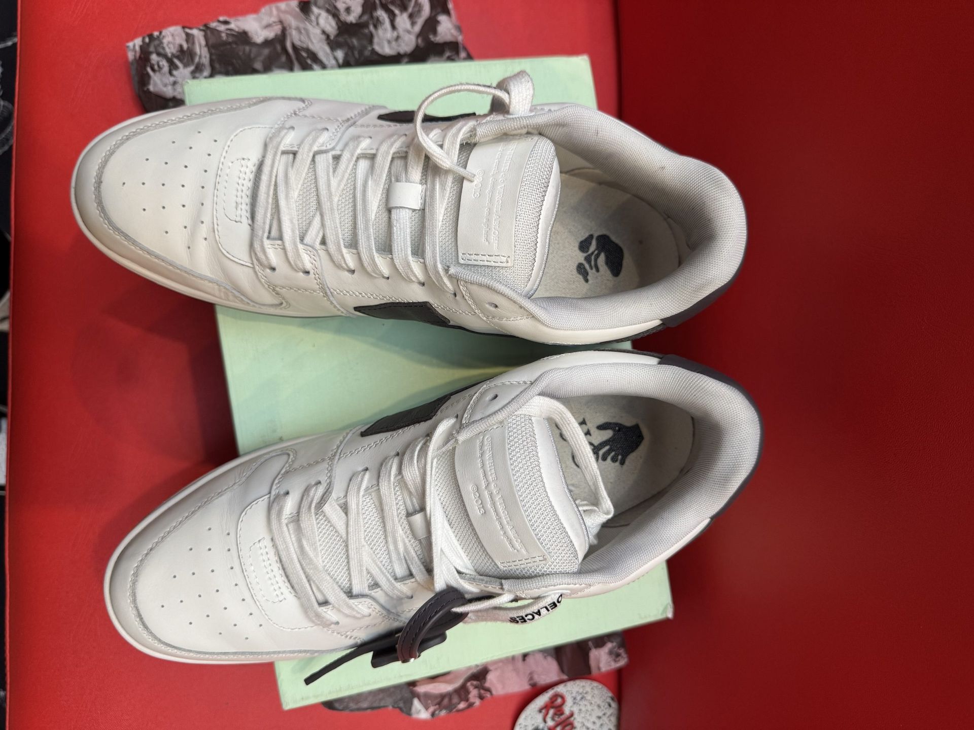 White and black sneaker with brown sole on a light green box, on a red surface.