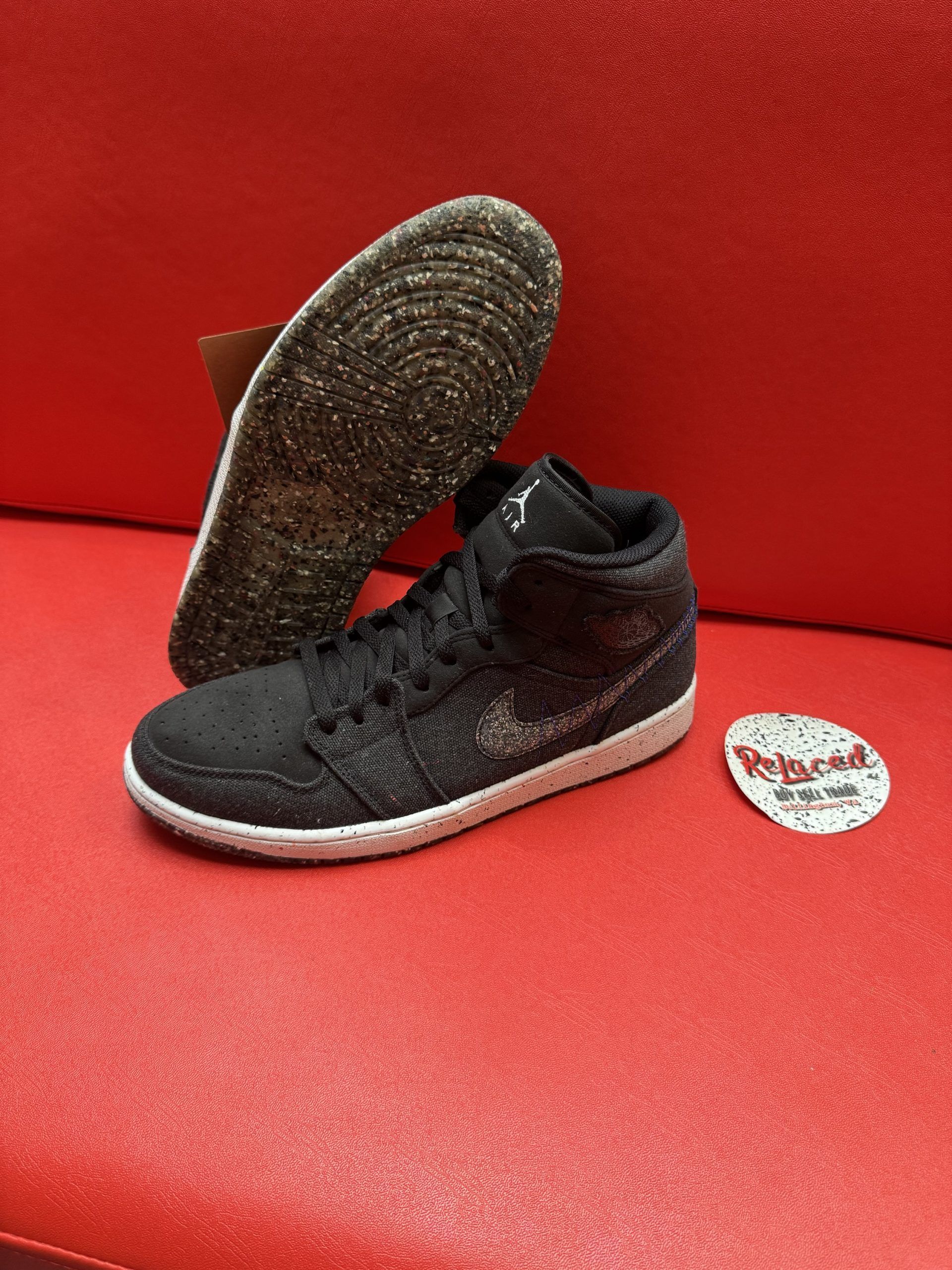 Black Nike Air Jordan sneaker with speckled sole on a red surface.