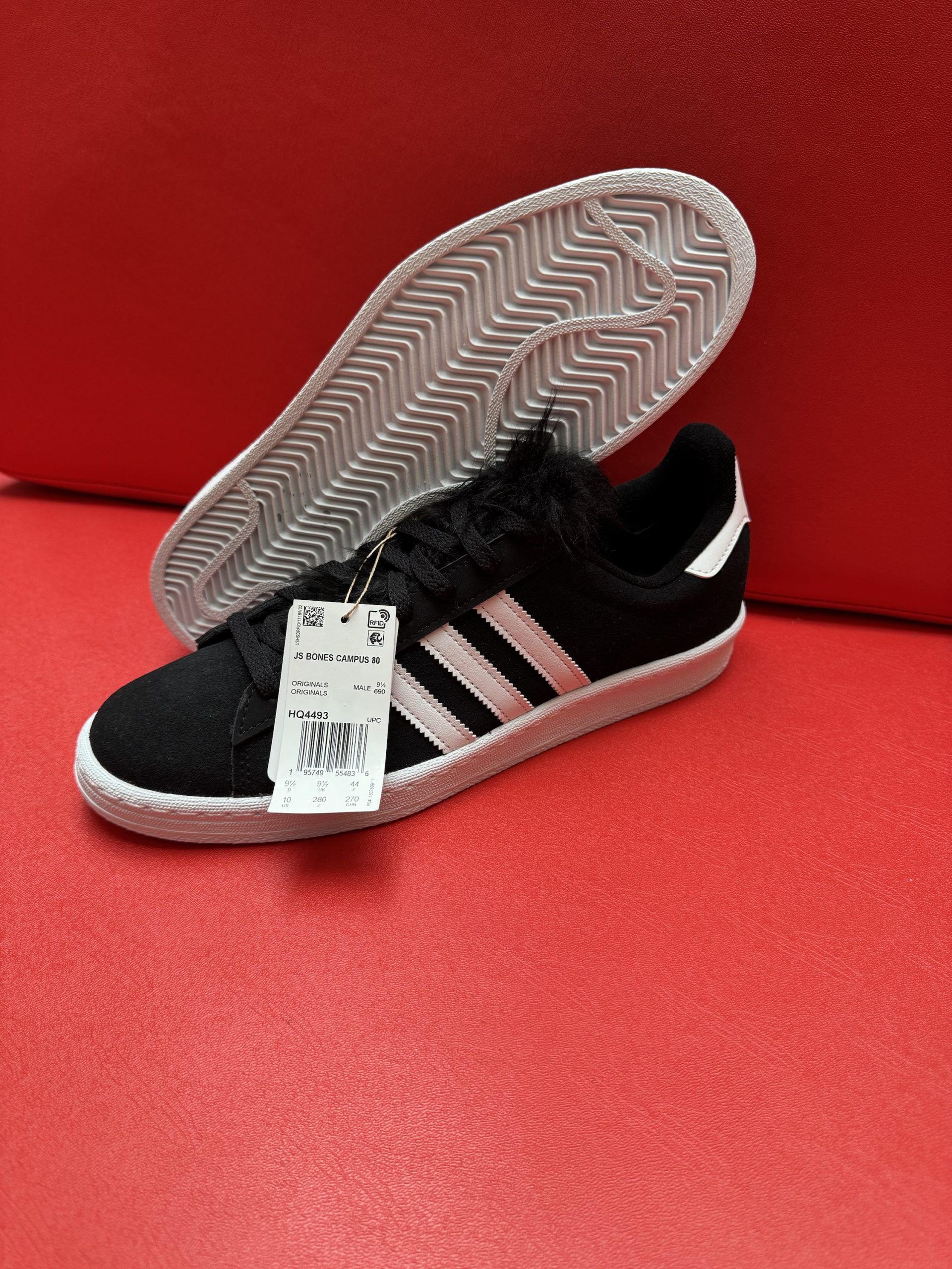 Black Adidas sneaker with pink stripes, white sole, and price tag on a red surface.