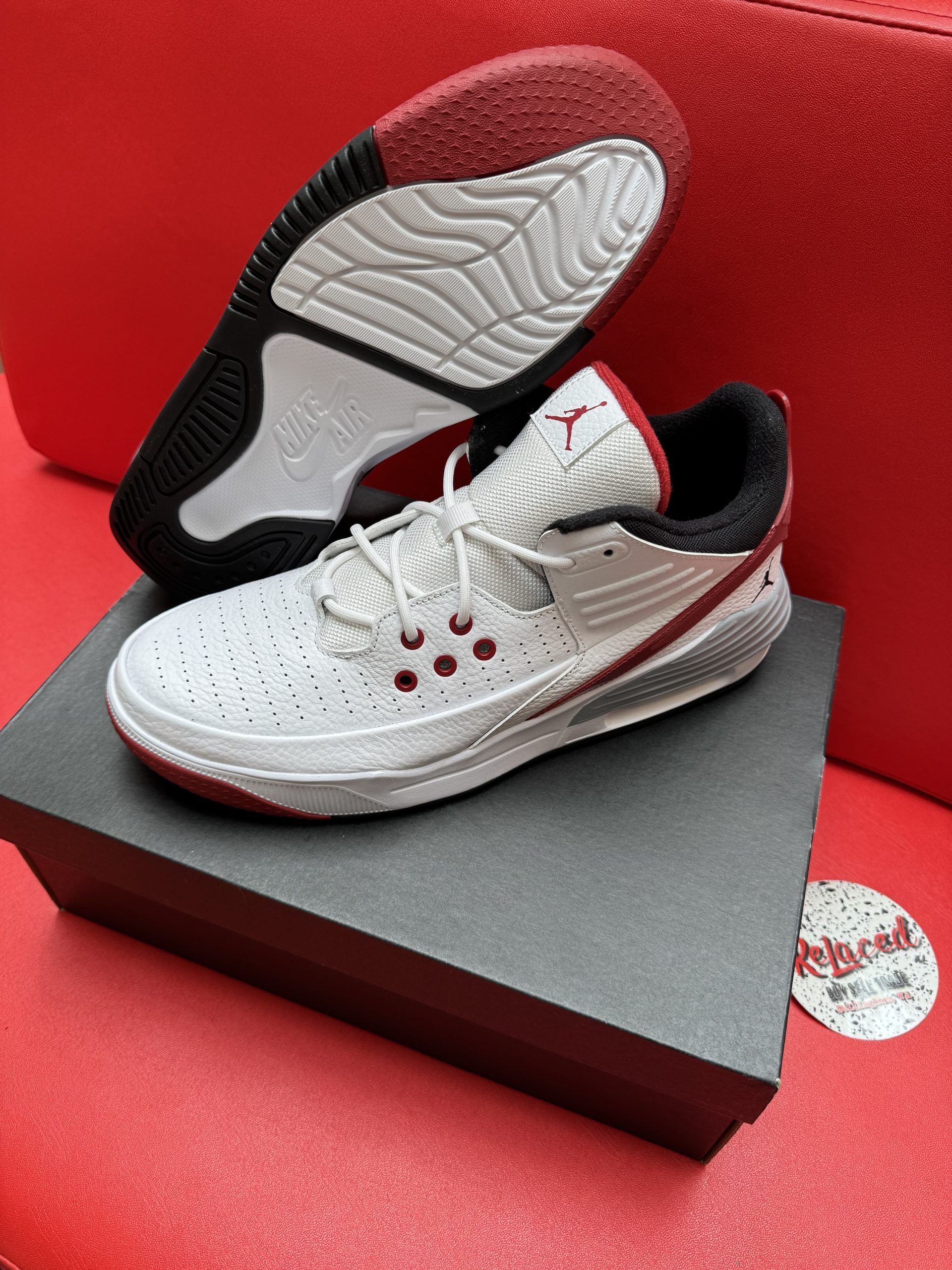 White and red Air Jordan basketball sneaker on a black box, with the sole visible, on a red surface.