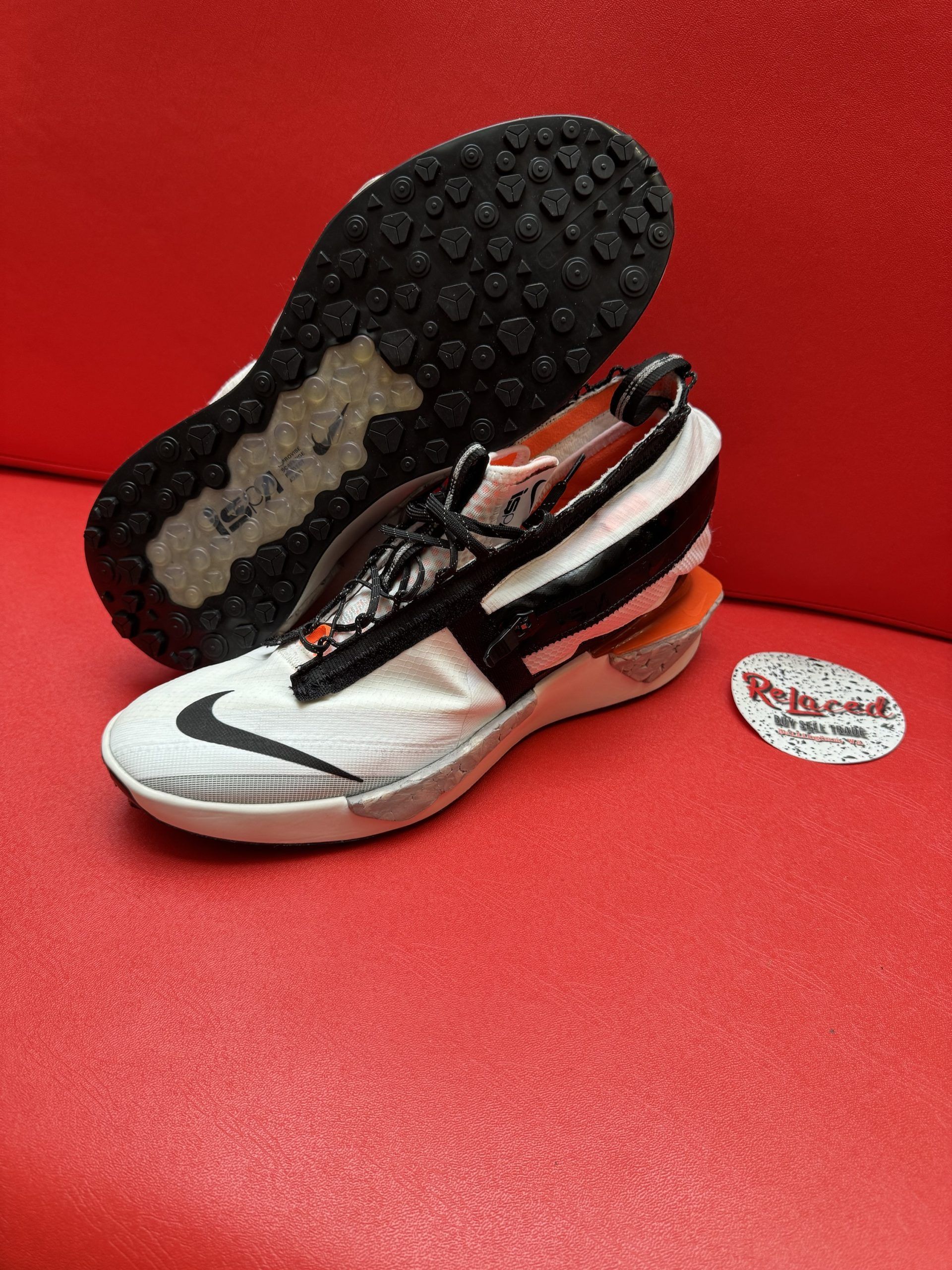 White and black Nike sneaker on a red surface with a black sole. A store label sits nearby.