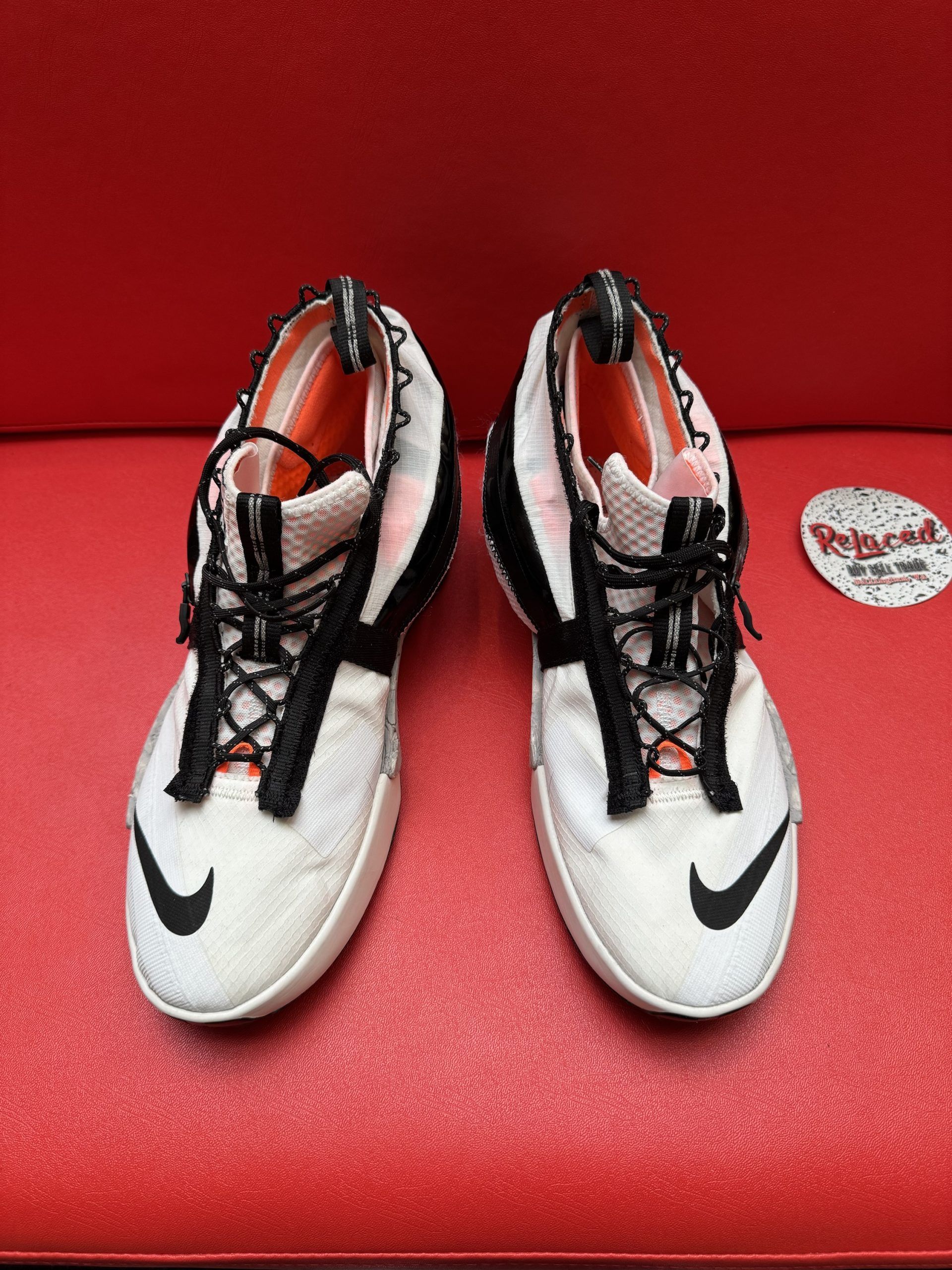 White and black Nike sneaker on a red surface with a black sole. A store label sits nearby.