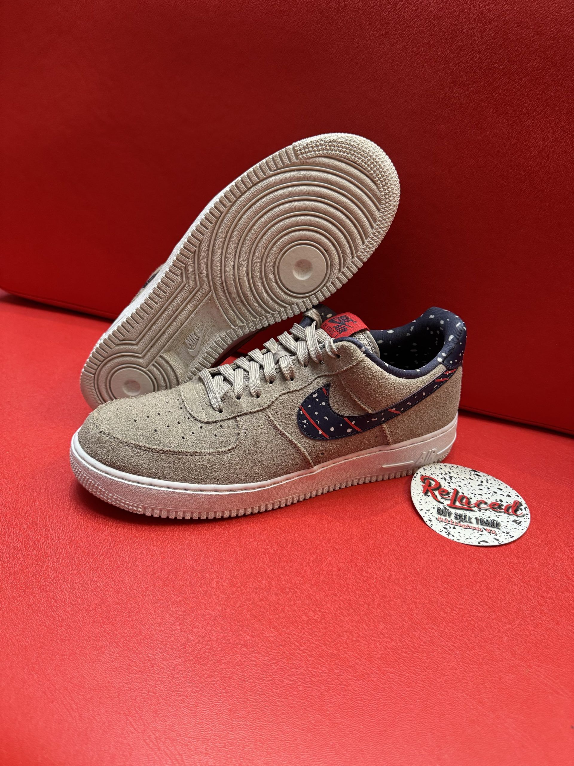 Tan Nike Air Force 1 sneakers with navy and white swoosh, lying on a red surface.