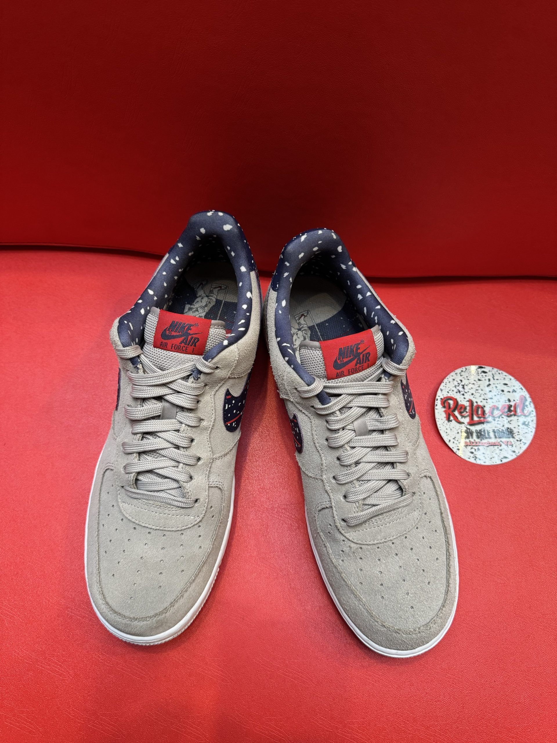 Tan Nike Air Force 1 sneakers with navy and white swoosh, lying on a red surface.