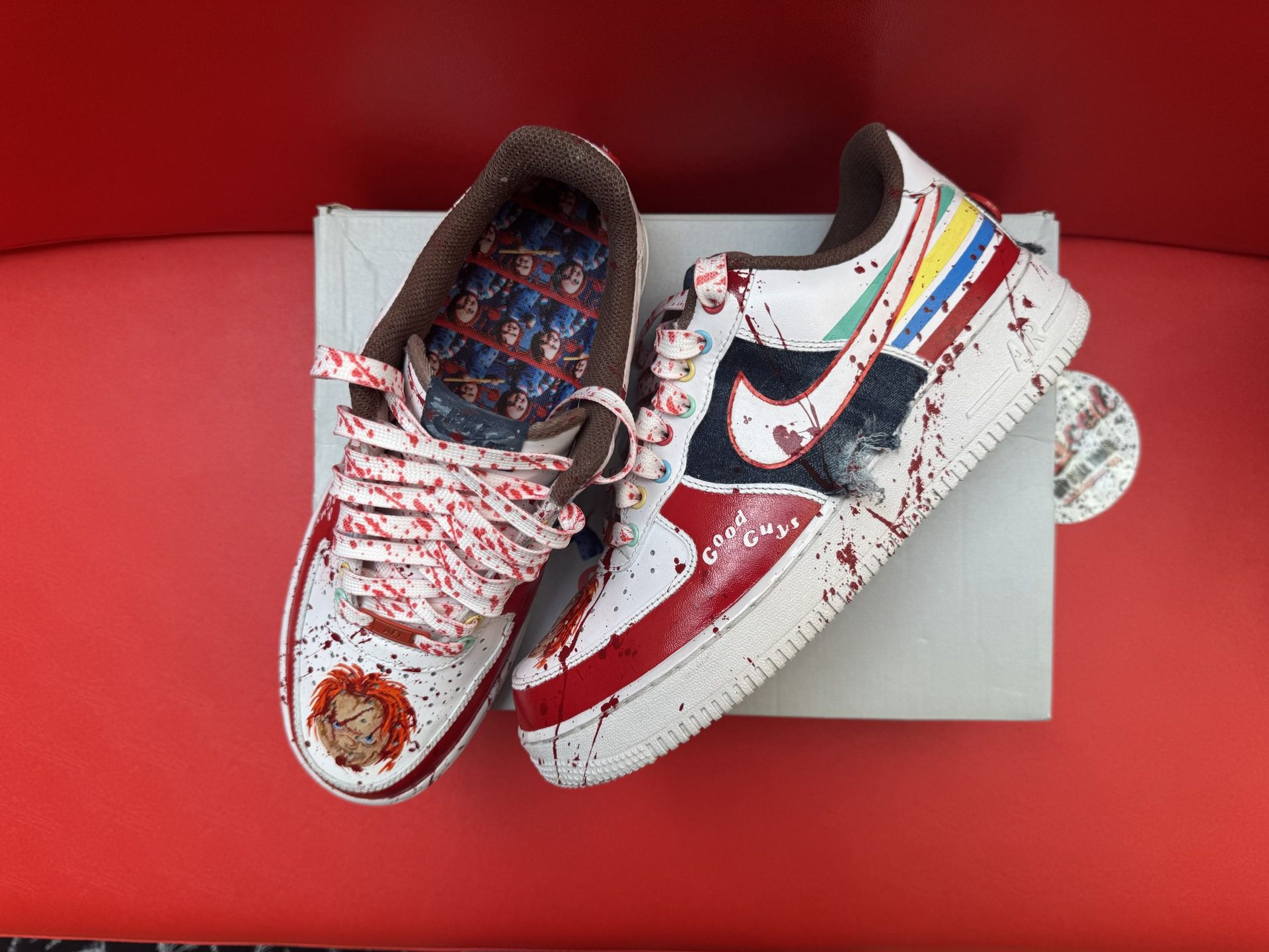 White Nike Air Force 1 sneakers, red blood splatter design, with Chucky image on the toe, resting on a box.