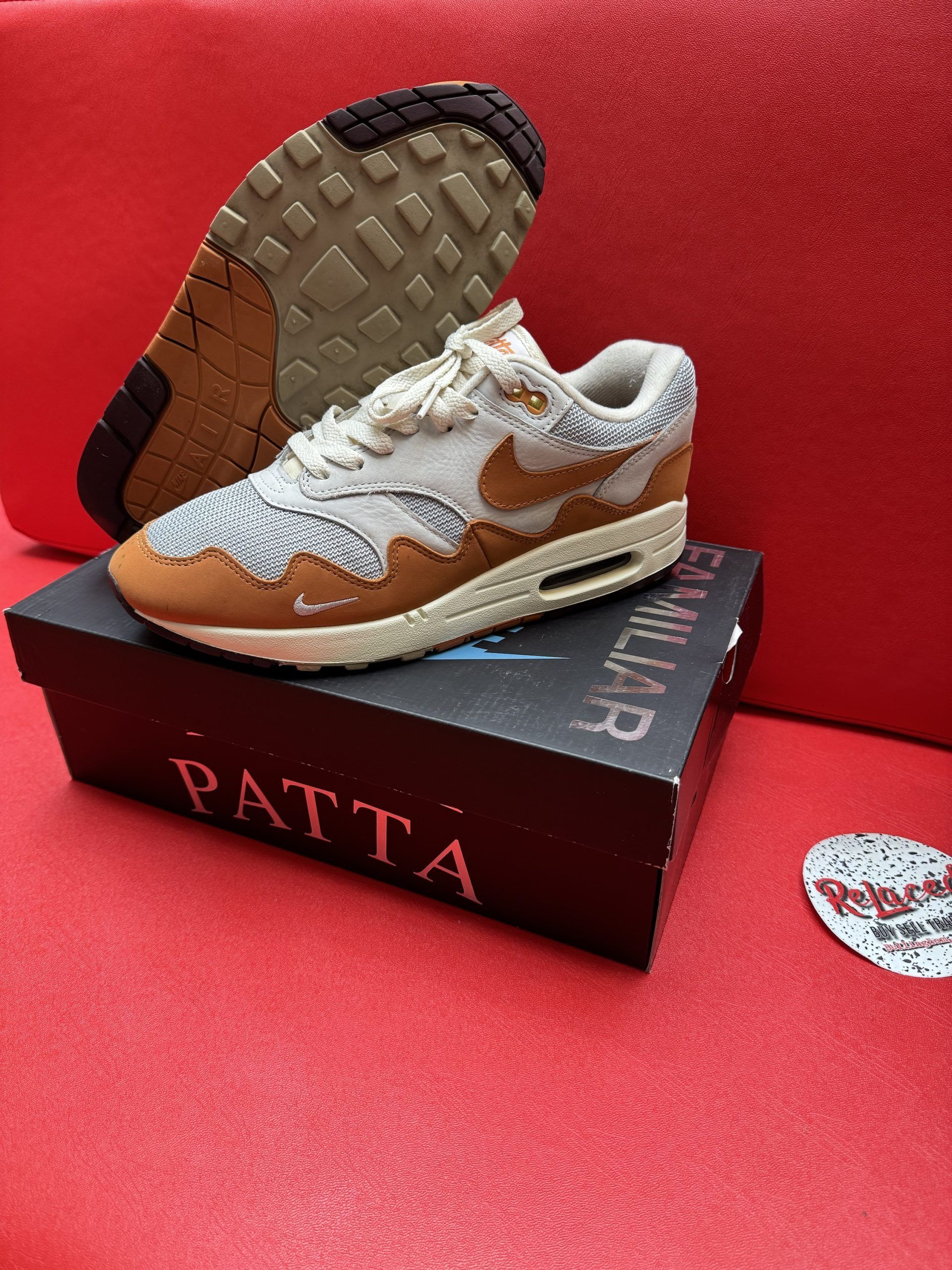 Nike Air Max 1 Patta sneakers on a box, with a brown outsole and tan, brown, and off-white accents on red surface.
