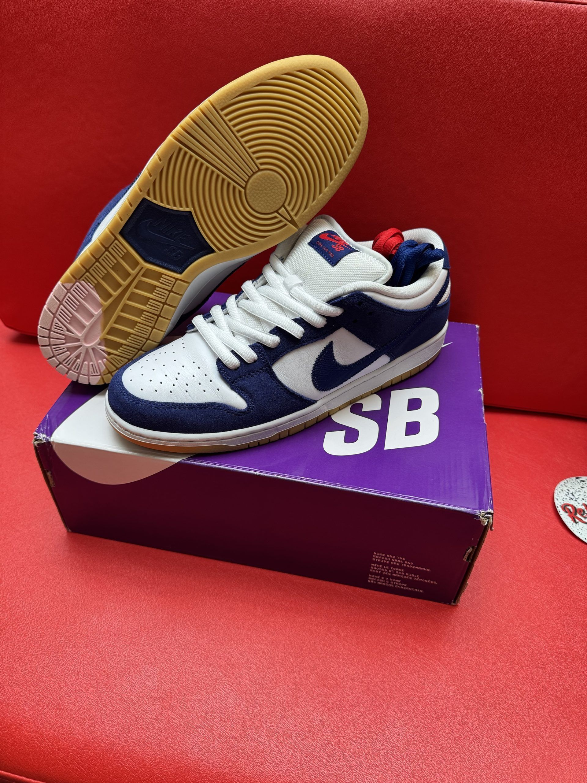 Nike SB Dunk Low sneakers in navy and white on a purple SB box, red surface, and a gum sole.