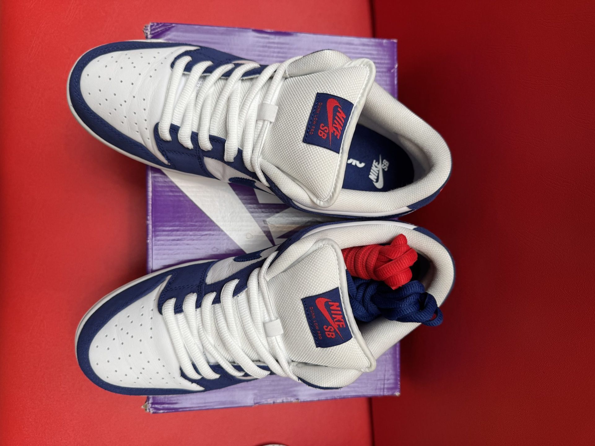 Nike SB Dunk Low sneakers in navy and white on a purple SB box, red surface, and a gum sole.