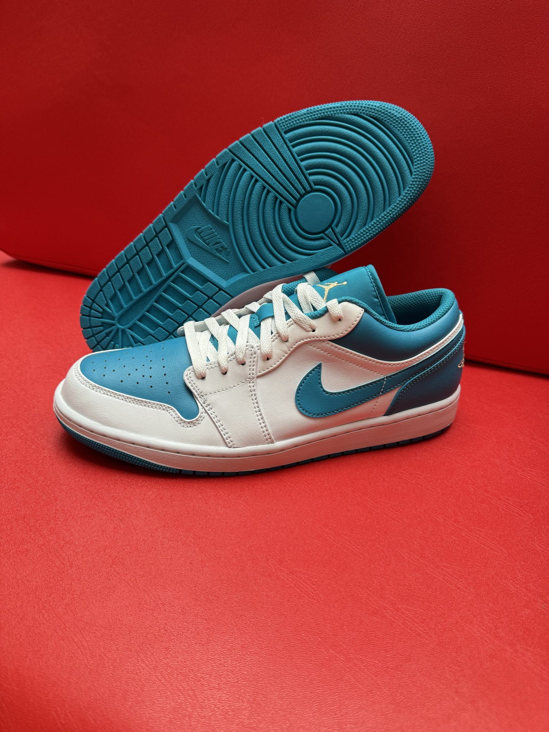 Teal and white Air Jordan low-top sneakers on a red surface, with one shoe's sole visible.
