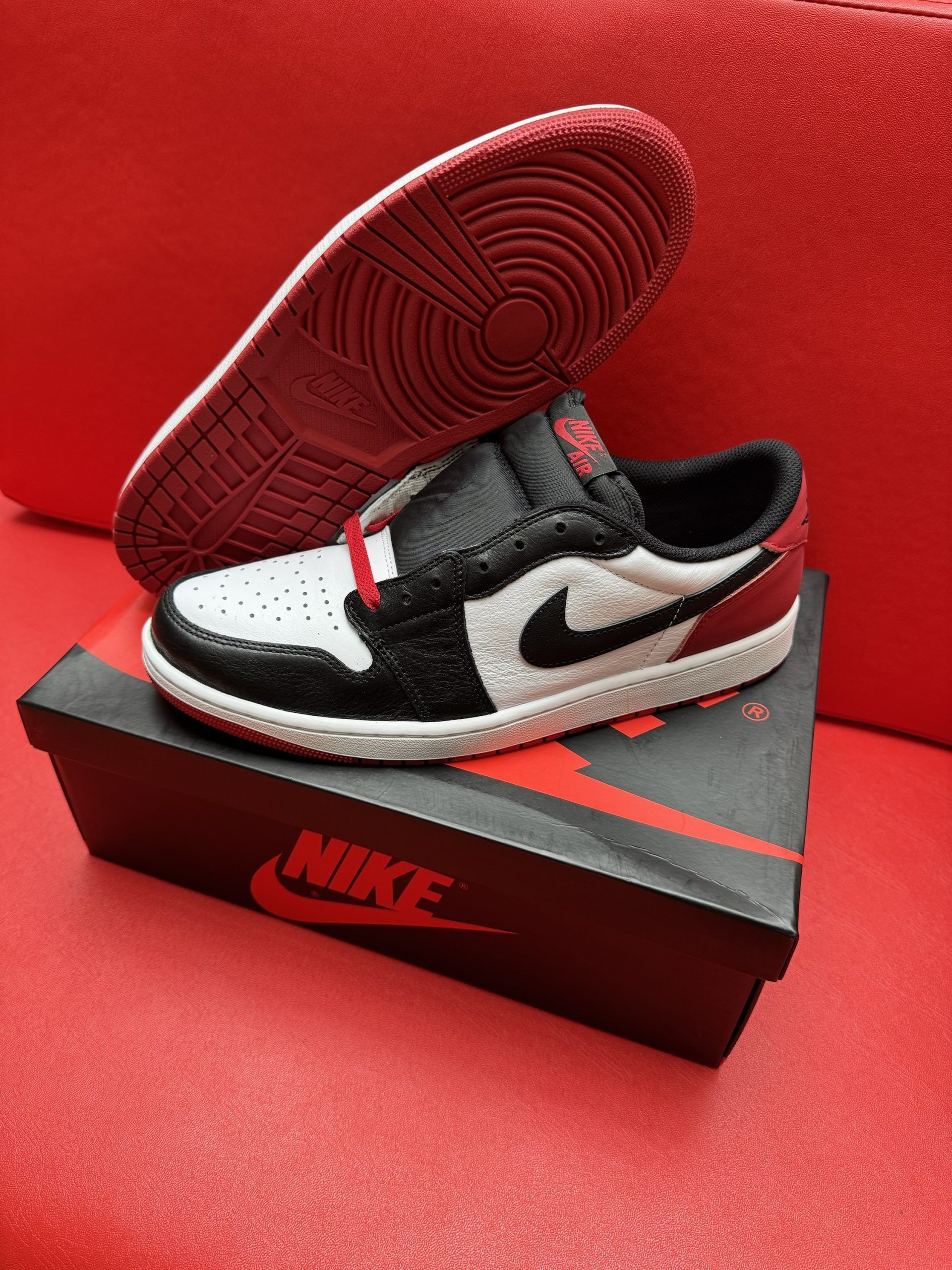 A child's Air Jordan 1 sneaker in black, white, and red on a shoebox. The sole is visible.