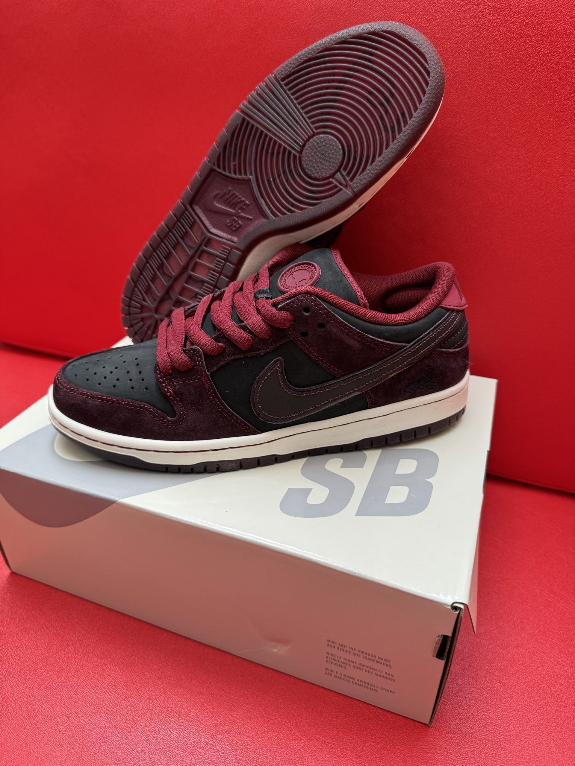 Nike SB Dunk low sneakers in black and burgundy on a white box with a burgundy sole visible.