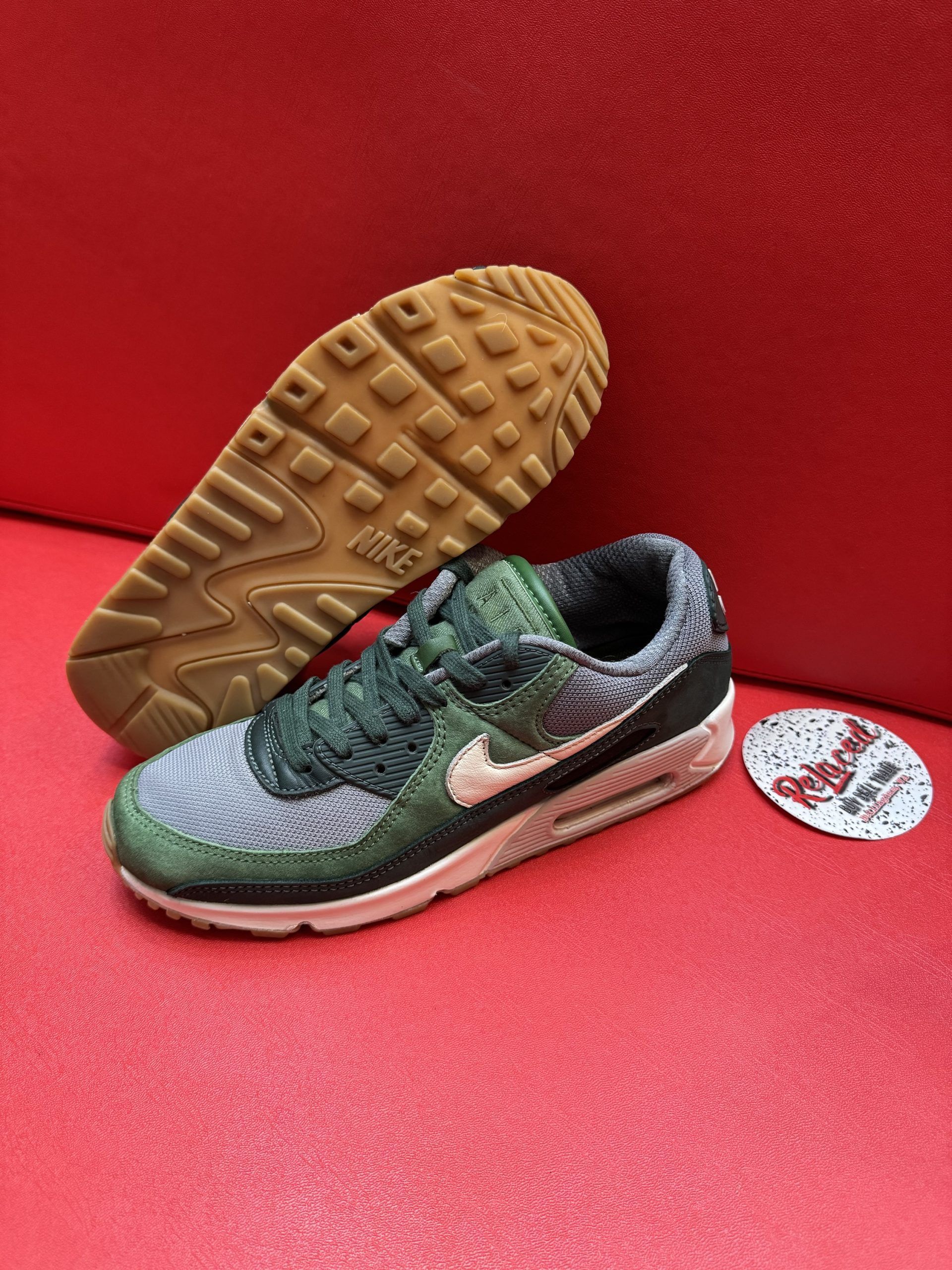 Green and gray Nike Air Max 90 sneaker with brown sole on red surface.