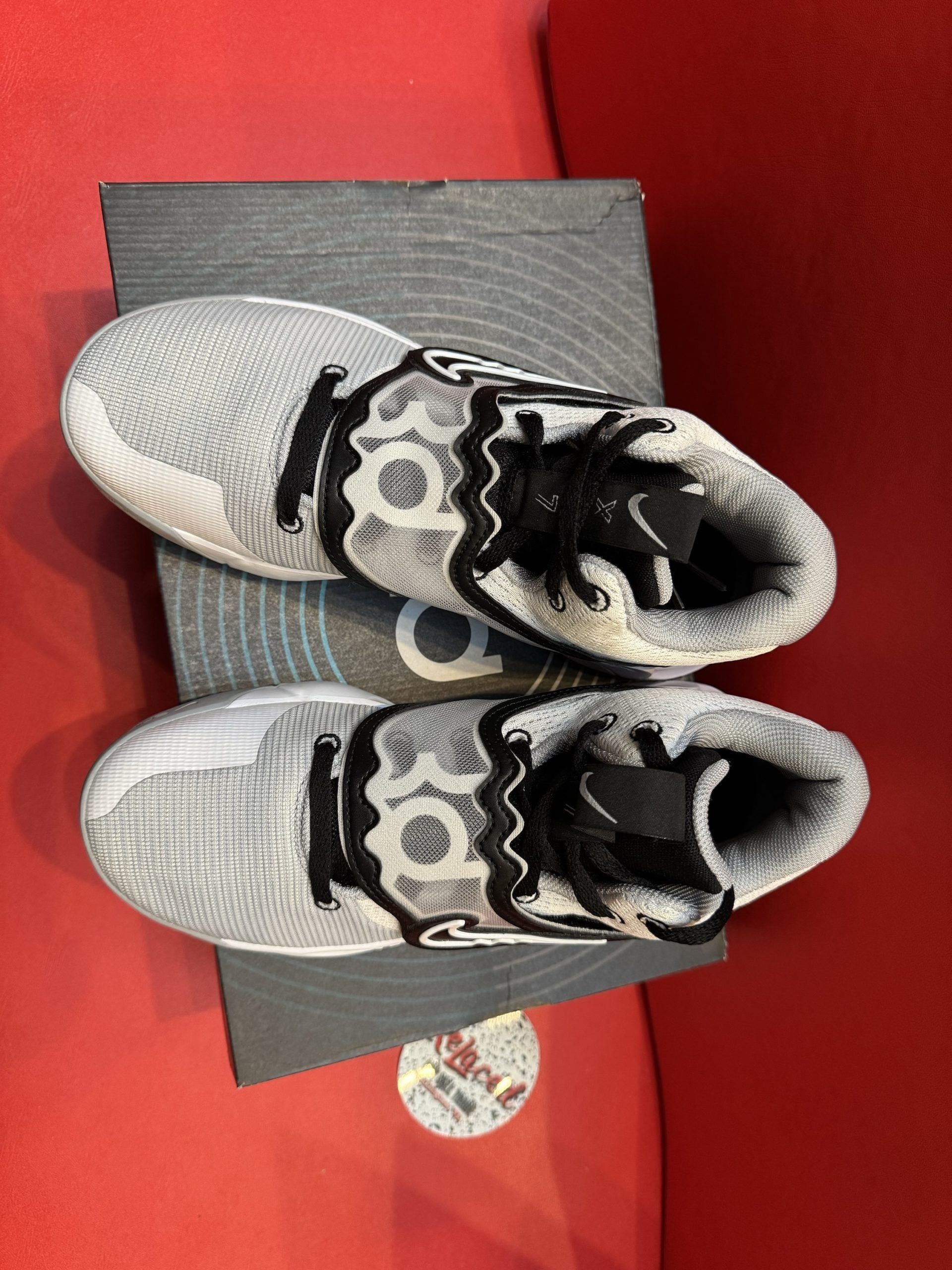 Basketball shoe on top of a shoe box. The shoe is white with black accents and a black swoosh. The sole is visible.