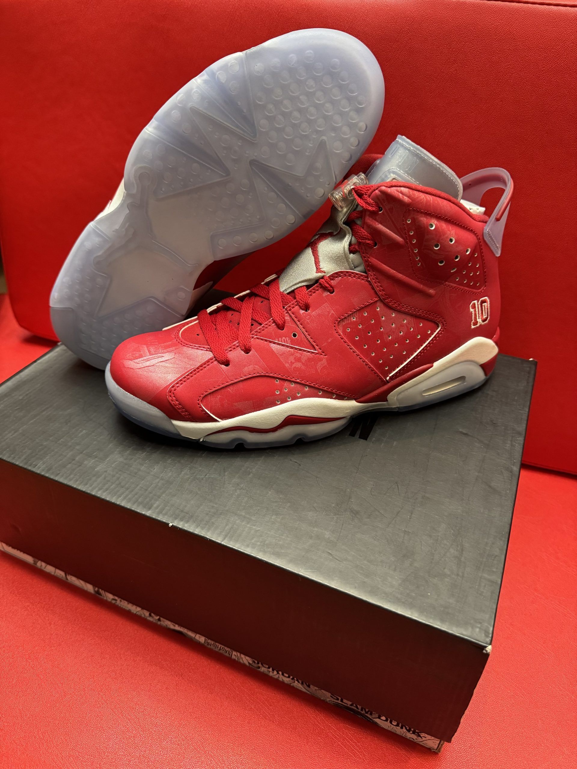 Red Air Jordan 6 sneakers, on a black box, with a clear sole, against a red background.