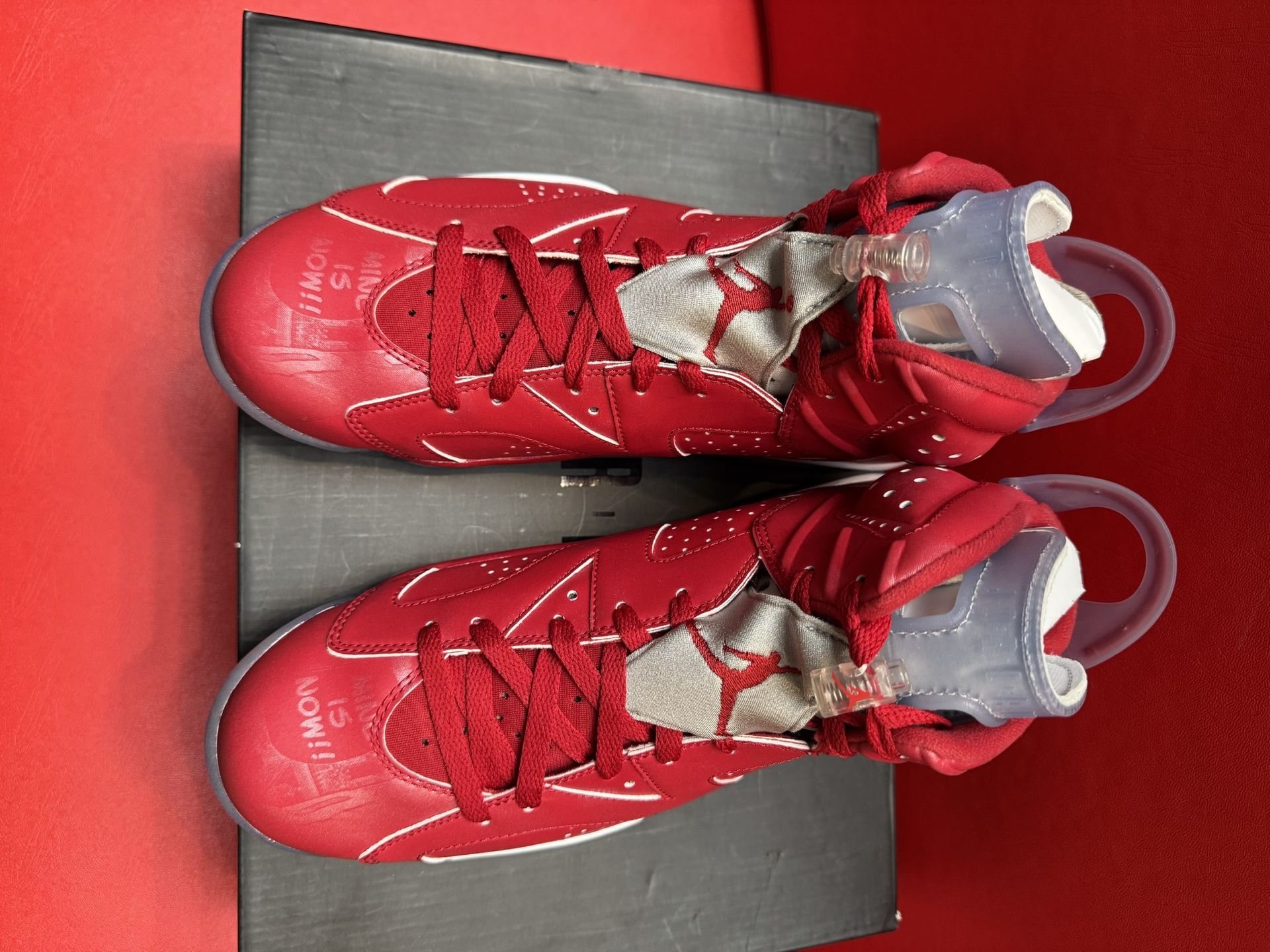 Red Air Jordan 6 sneakers, on a black box, with a clear sole, against a red background.