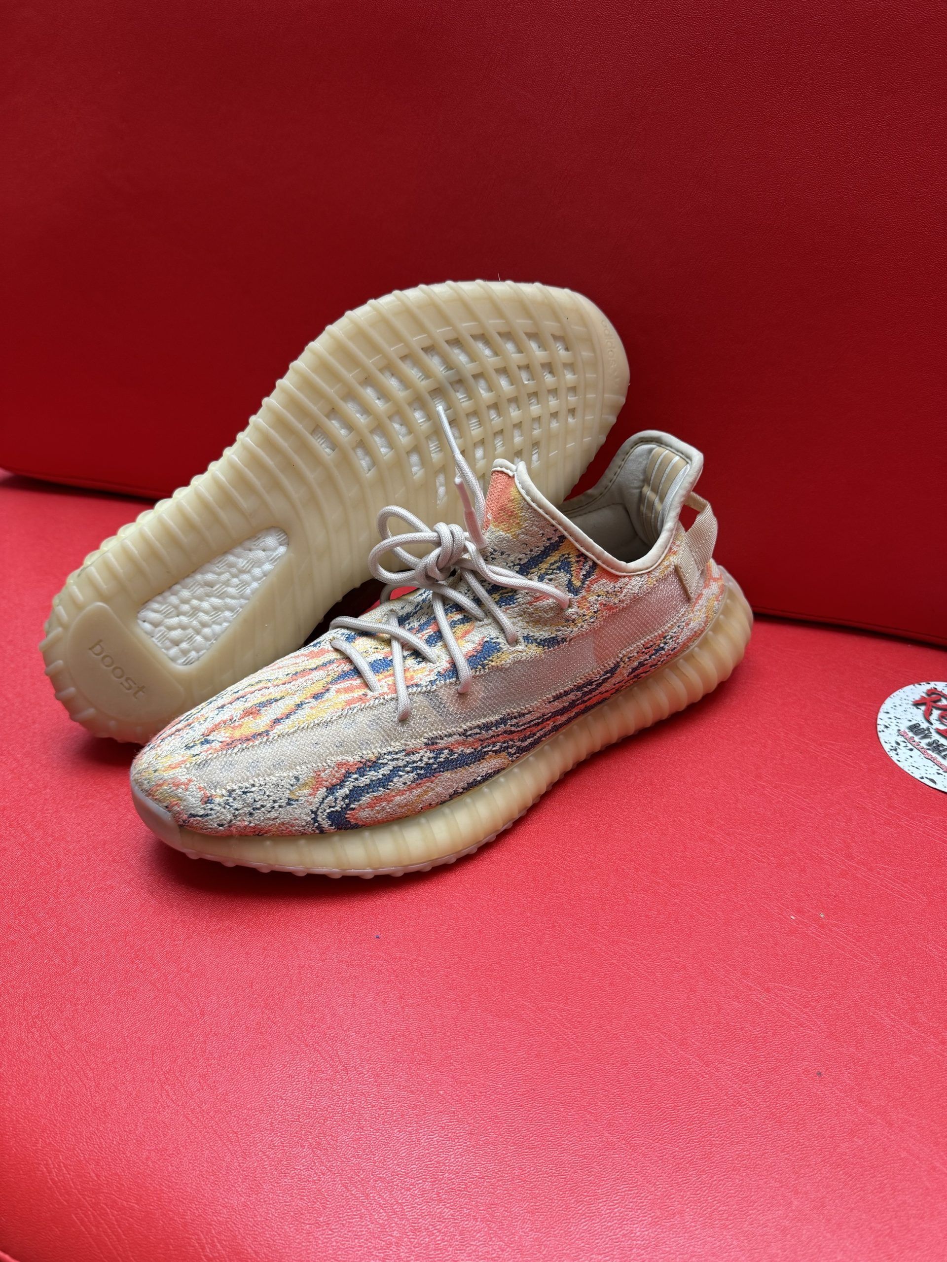 Yeezy Boost 350 V2 sneakers on a red surface, featuring a multi-colored knit upper and gum sole.
