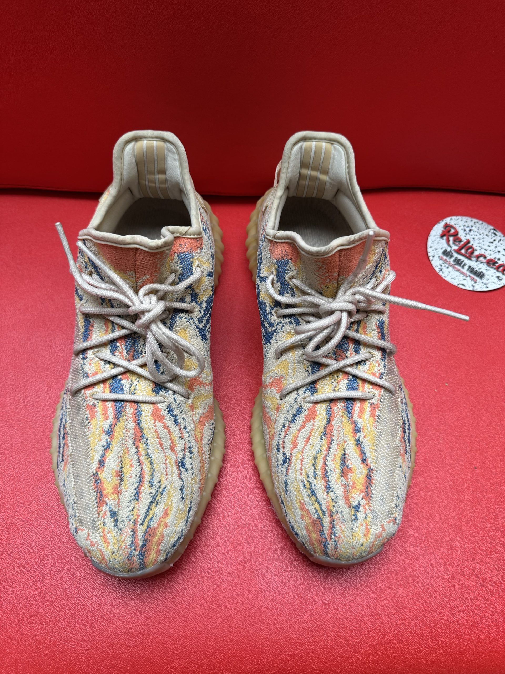 Yeezy Boost 350 V2 sneakers on a red surface, featuring a multi-colored knit upper and gum sole.