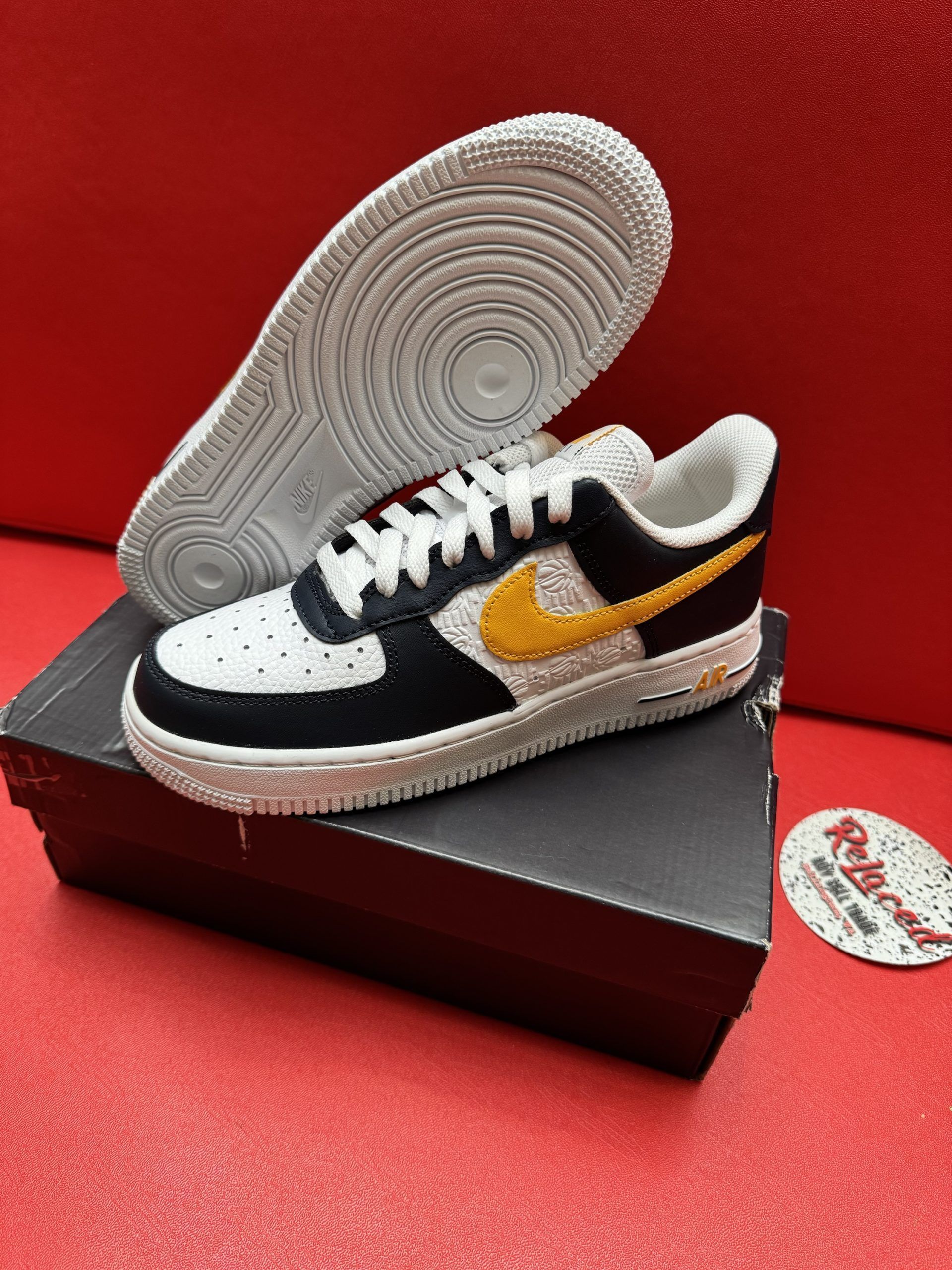 Black, white, and gold Nike Air Force 1 sneaker on top of a shoebox, with white sole visible.