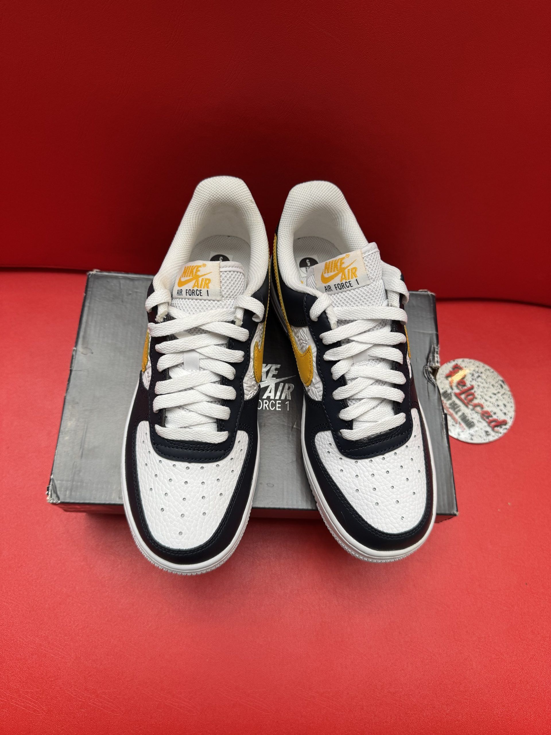 Black, white, and gold Nike Air Force 1 sneaker on top of a shoebox, with white sole visible.