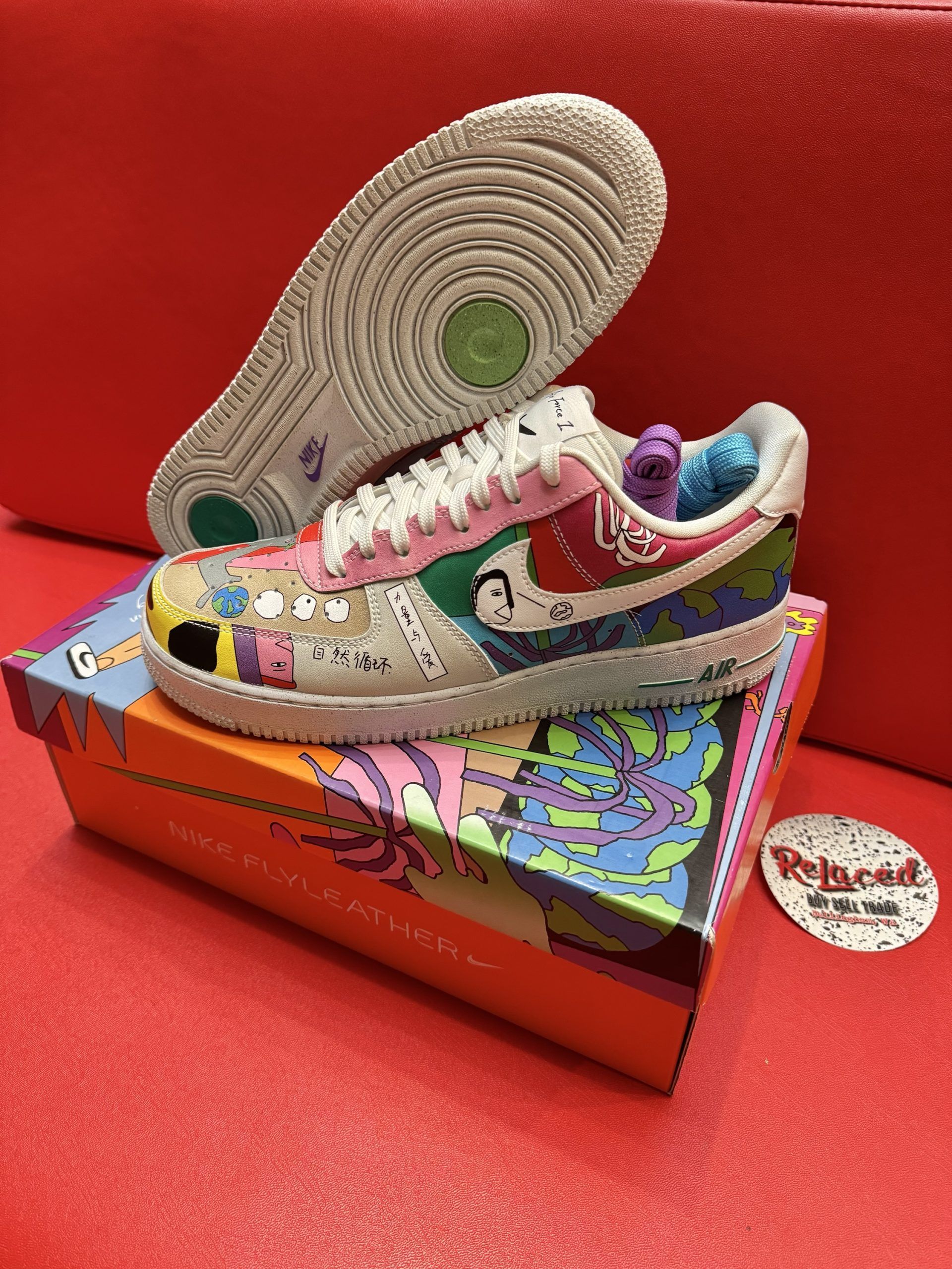 Customized Nike Air Force 1 sneaker with colorful artwork, displayed on its box and a red surface.