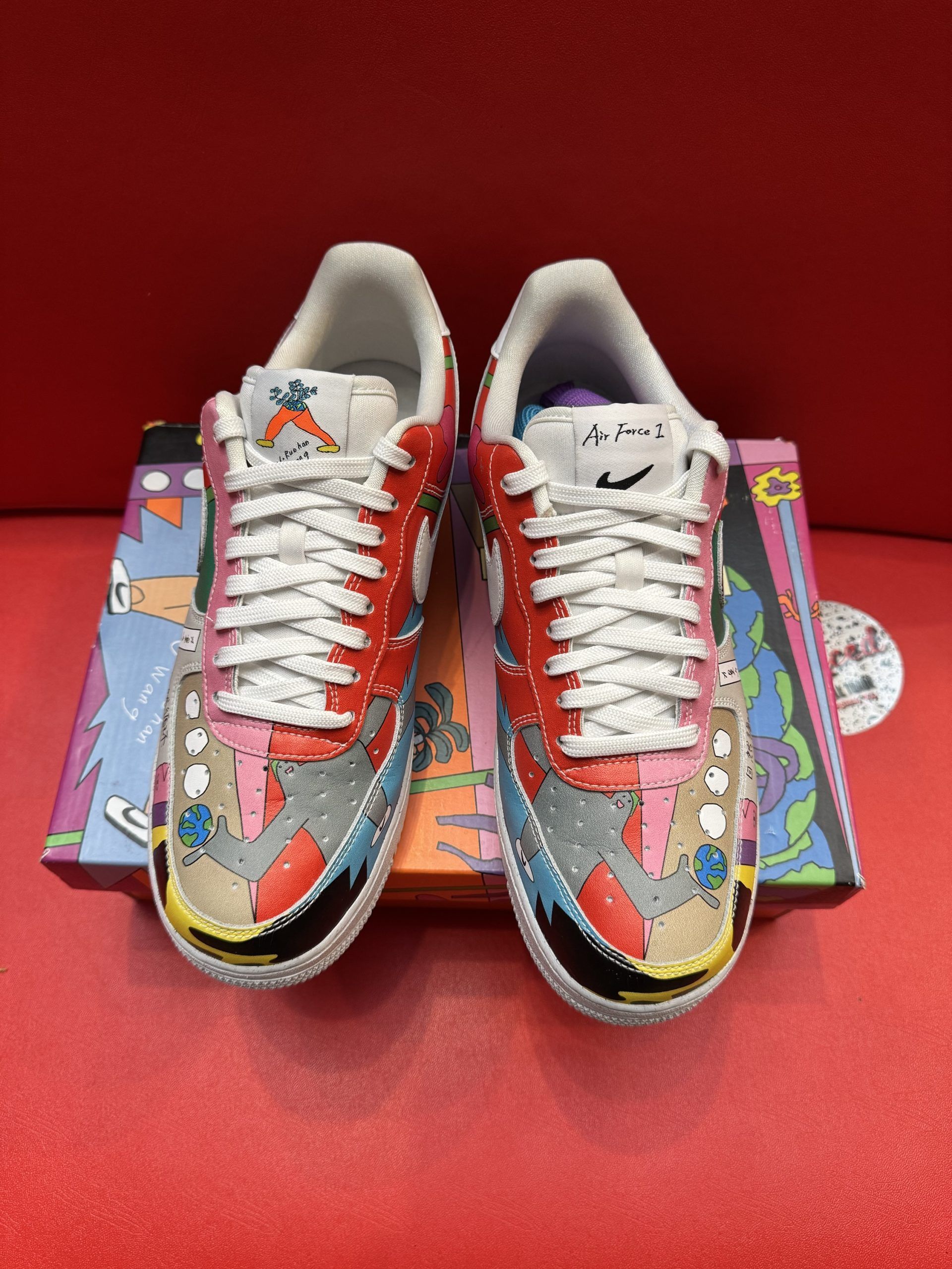 Customized Nike Air Force 1 sneaker with colorful artwork, displayed on its box and a red surface.