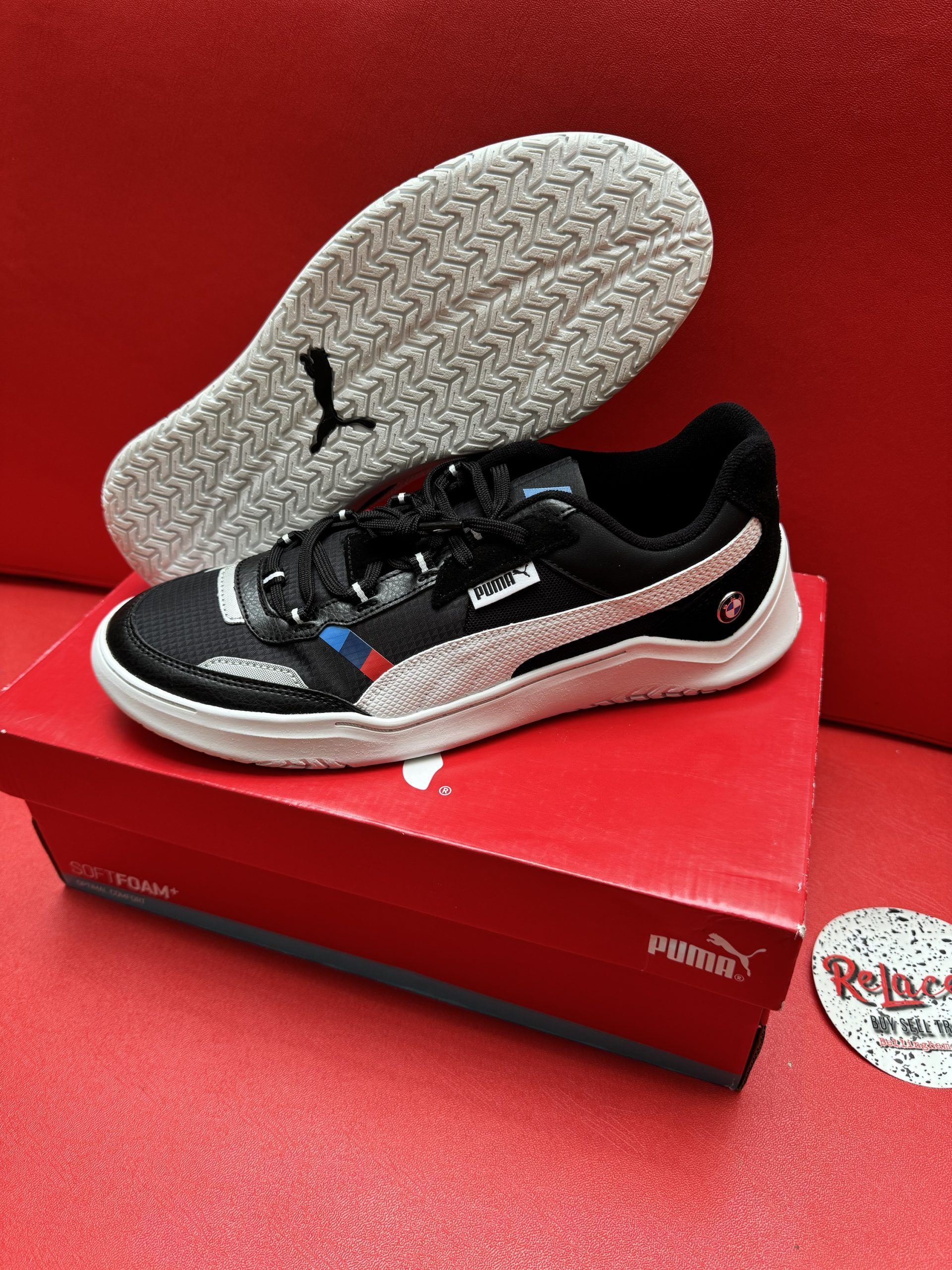 Black Puma shoe with white stripe, on red box and background. The sole is visible.