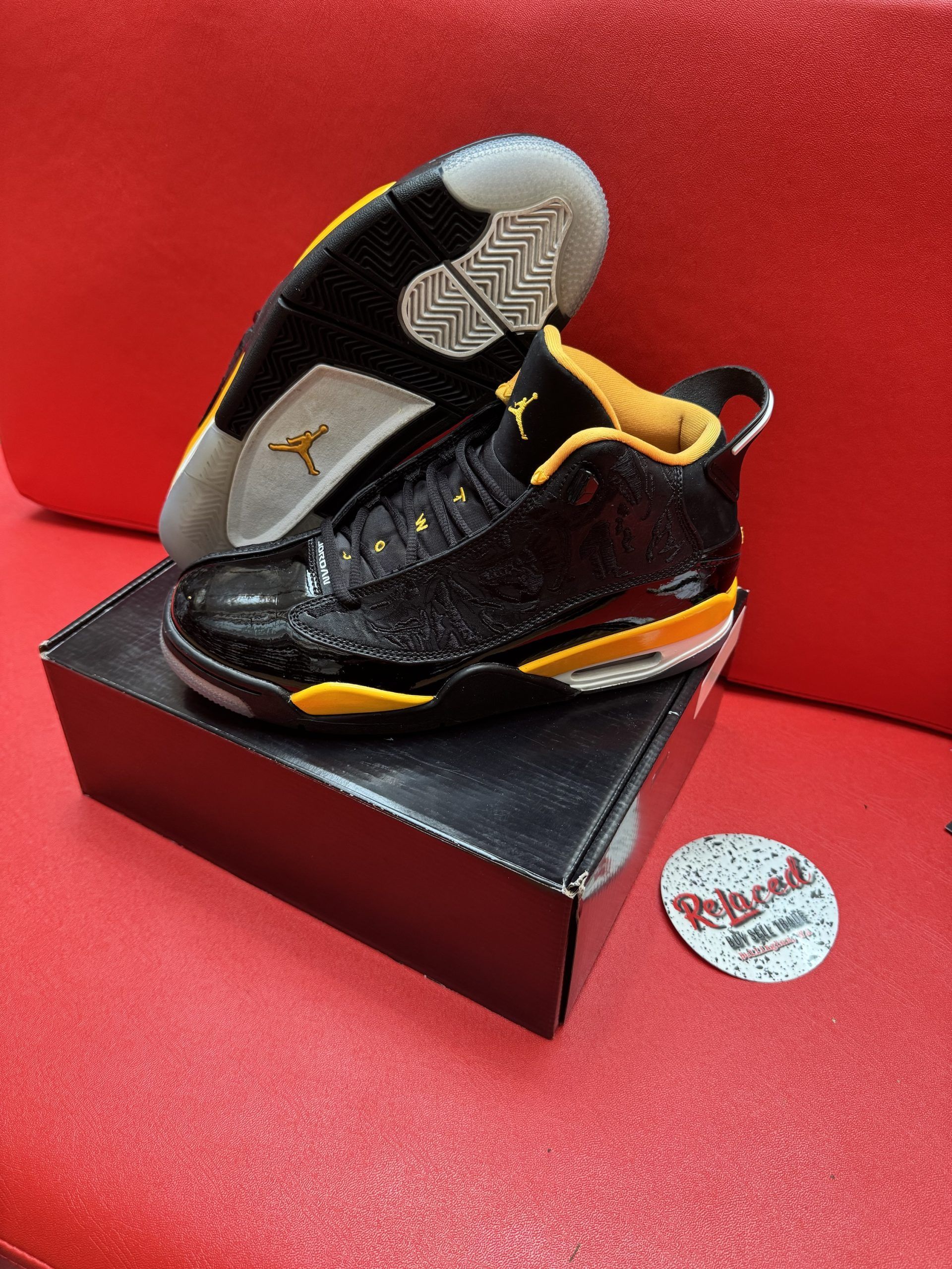 Black and yellow Air Jordan sneakers on a black box, with a red background and a logo sticker.