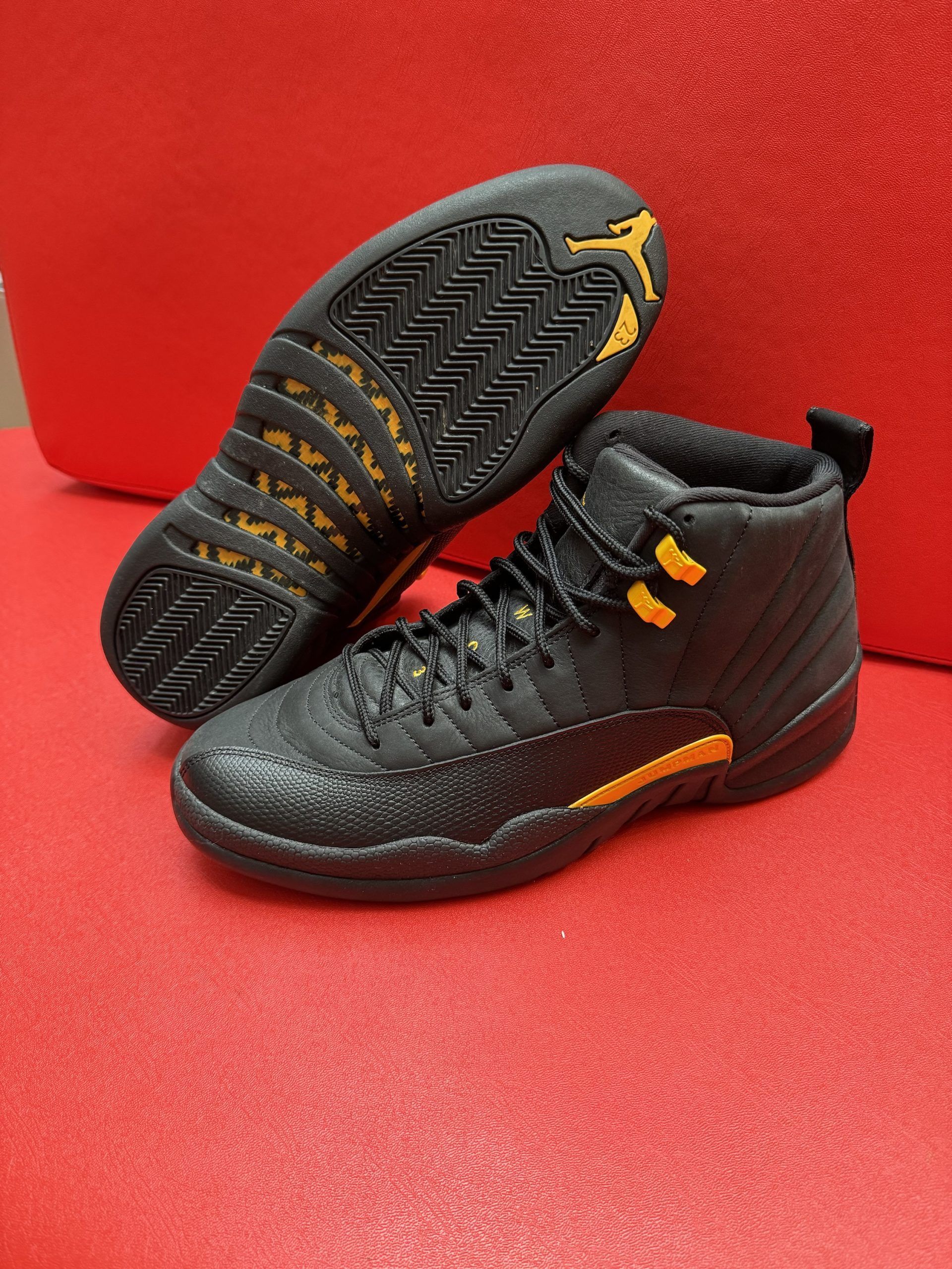 Black and yellow Air Jordan 12 sneakers, set on a red surface.