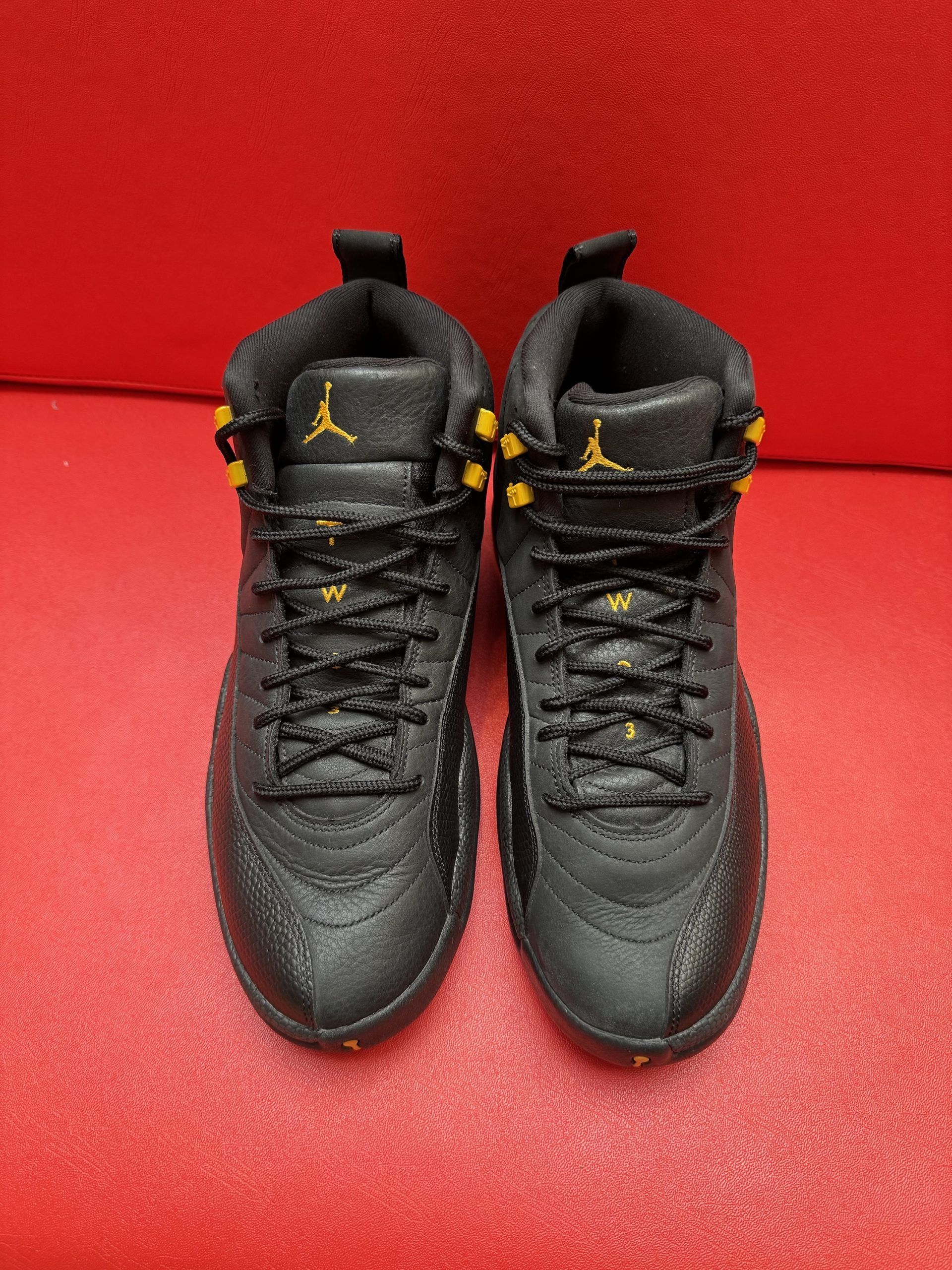 Black and yellow Air Jordan 12 sneakers, set on a red surface.