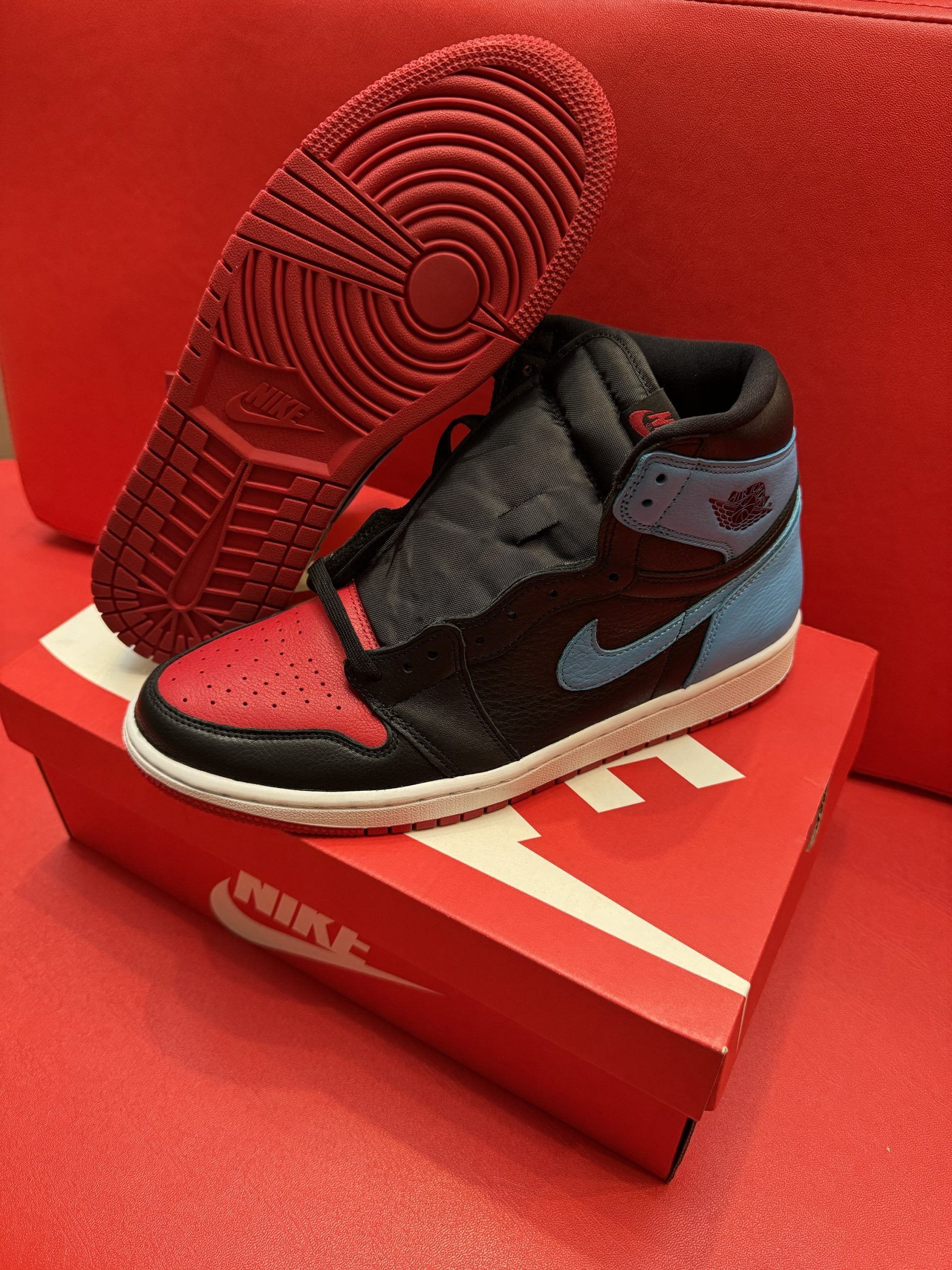 Air Jordan 1 sneaker with red toe and outsole, black midfoot, blue collar, sitting on red Nike shoebox.