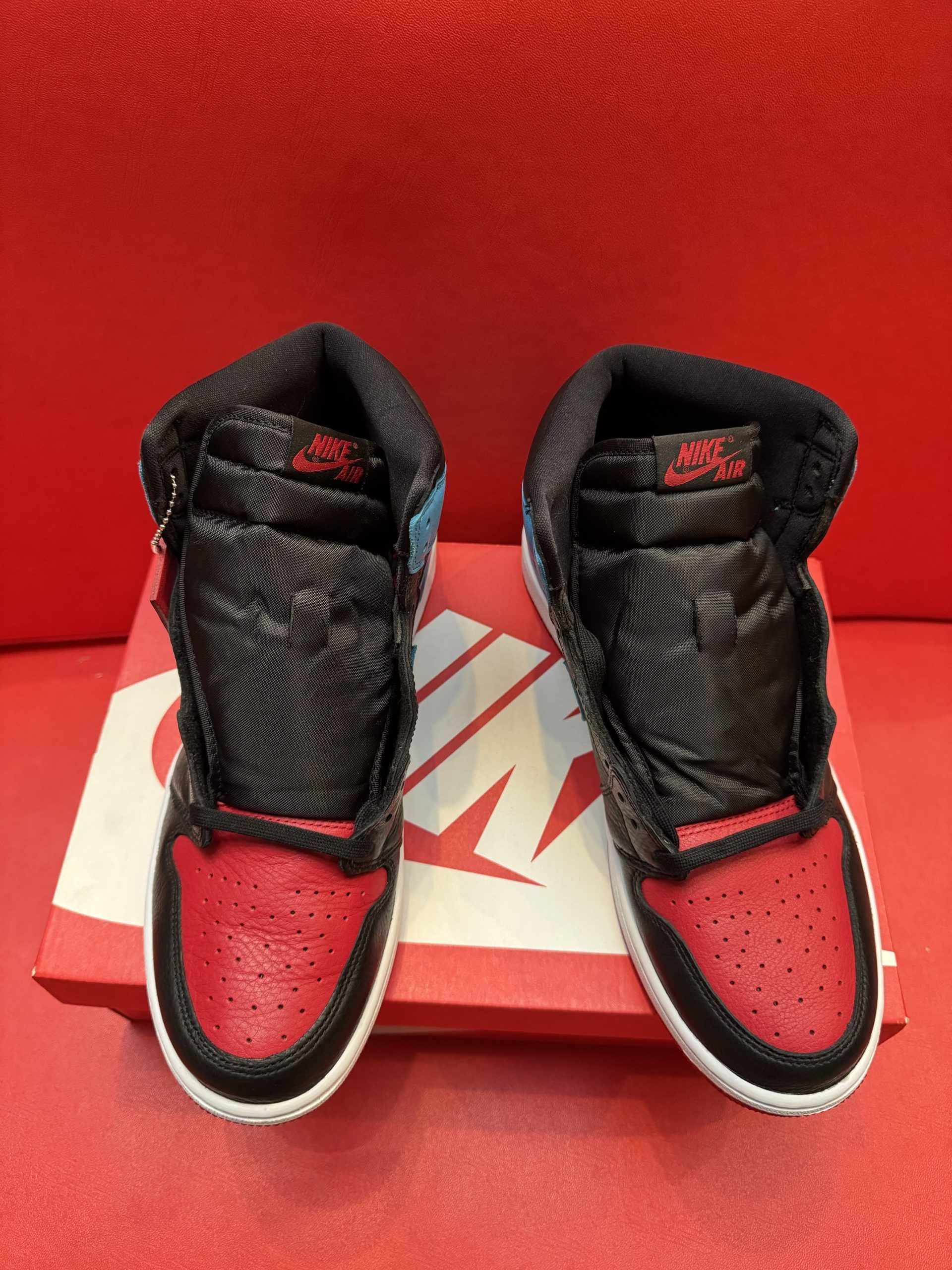 Air Jordan 1 sneaker with red toe and outsole, black midfoot, blue collar, sitting on red Nike shoebox.