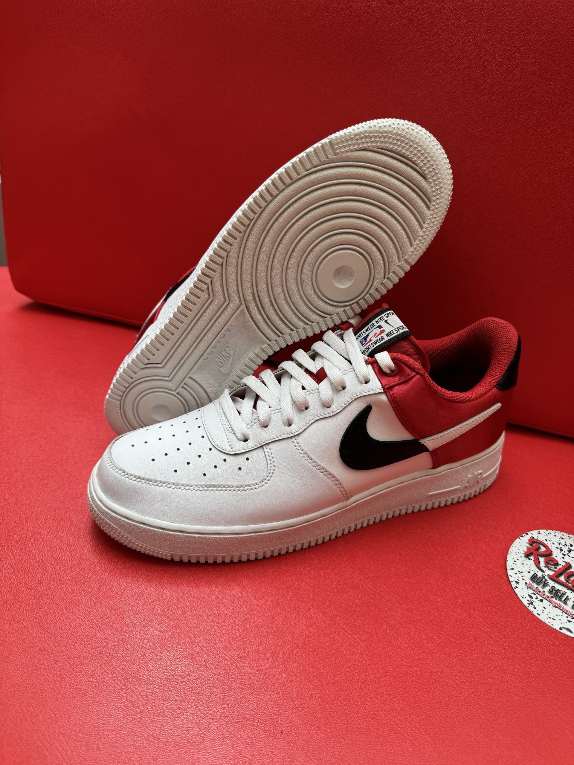 White and red Nike Air Force 1 sneakers on a red surface, one upside down.