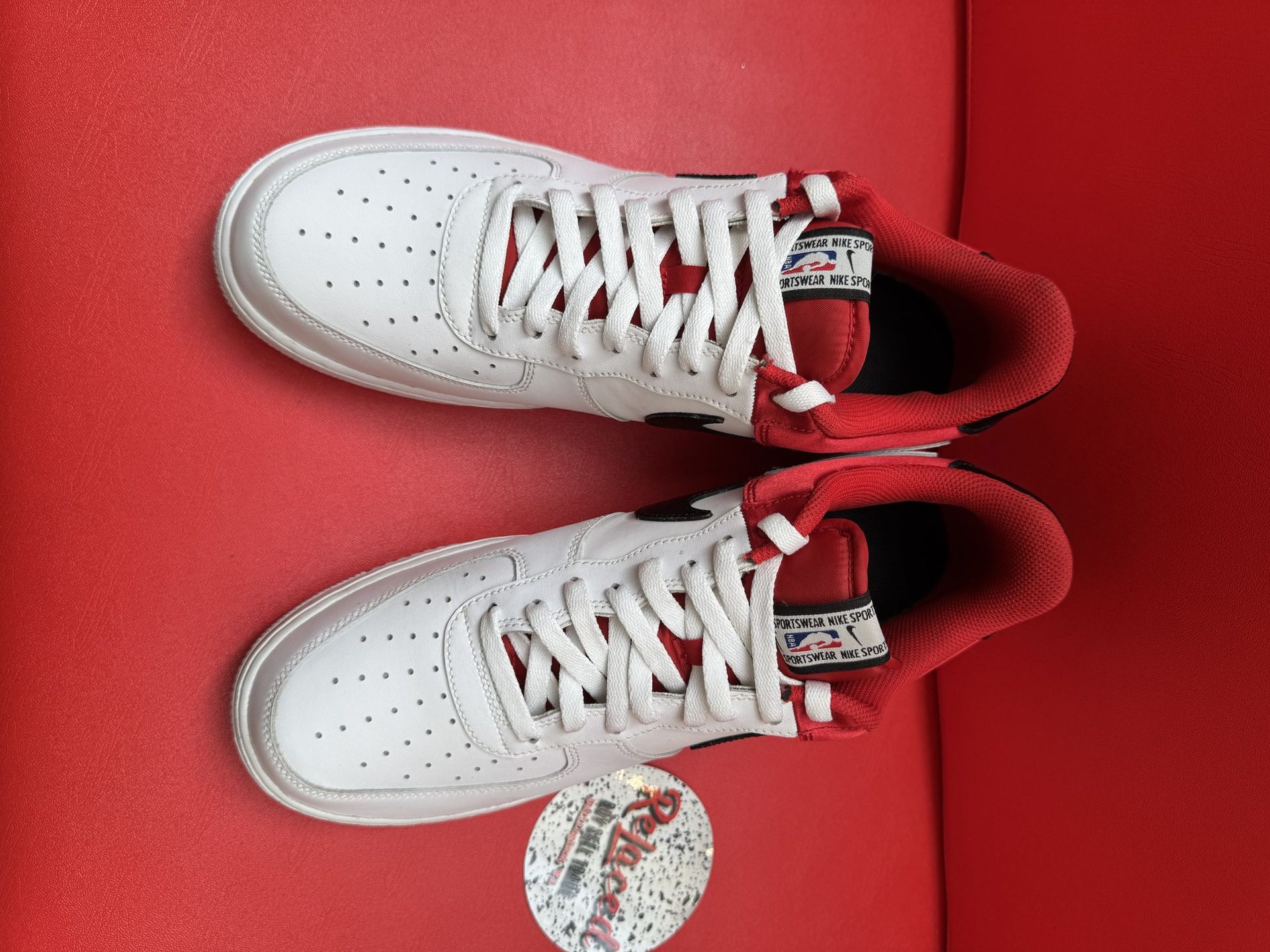 White and red Nike Air Force 1 sneakers on a red surface, one upside down.