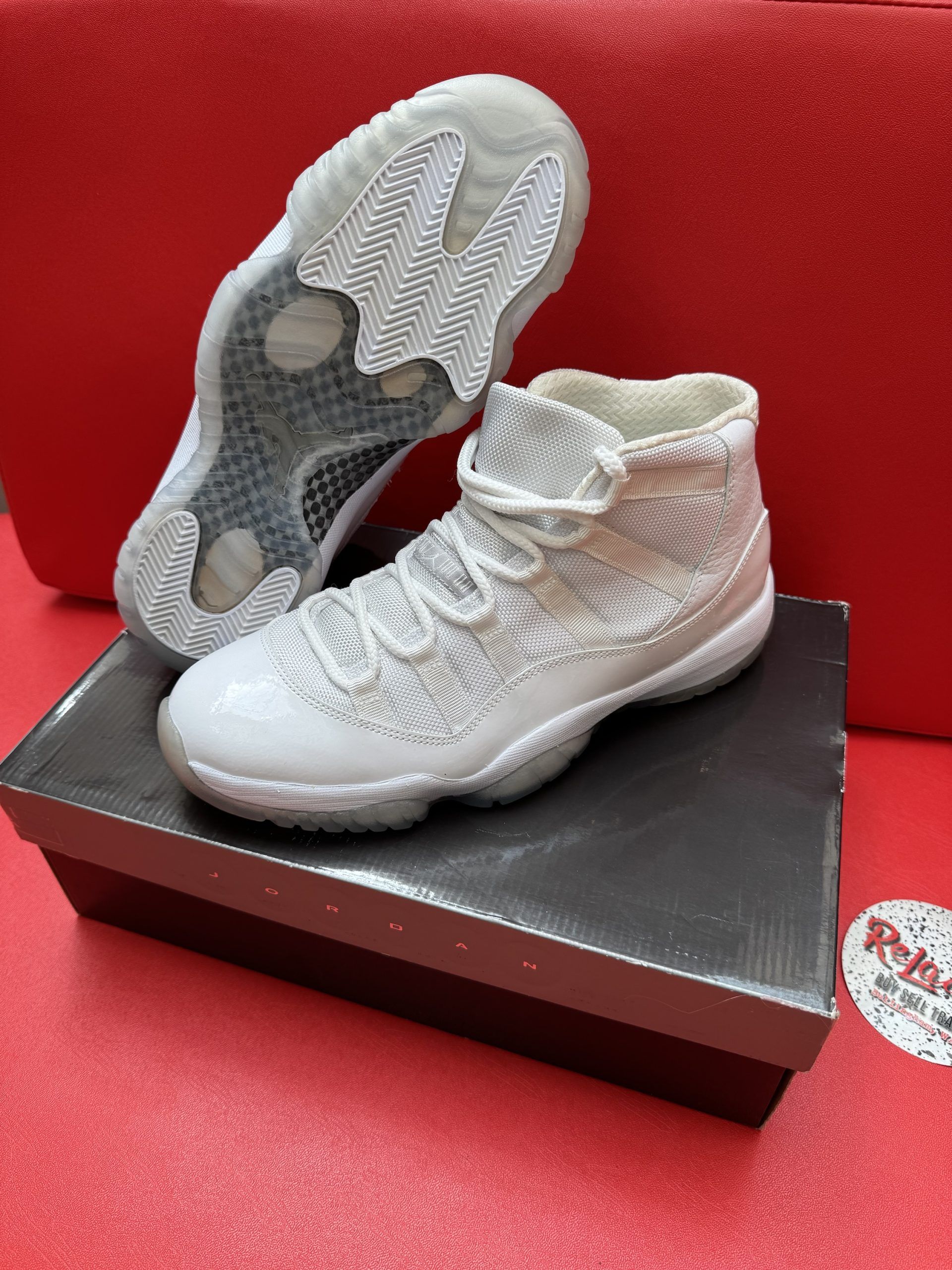 White high-top sneakers on a shoebox. Clear soles, textured design, and laces. Red background.