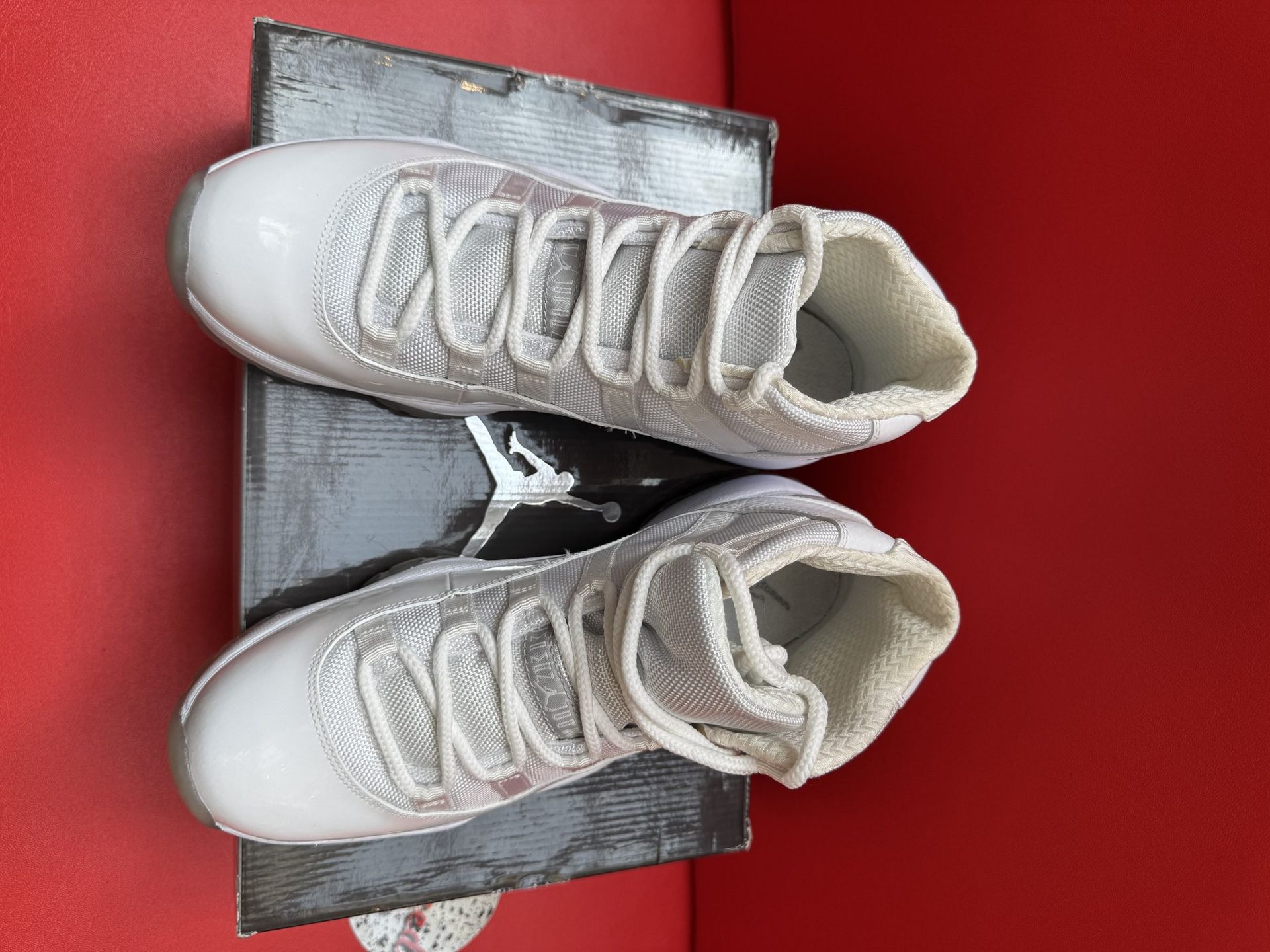 White high-top sneakers on a shoebox. Clear soles, textured design, and laces. Red background.