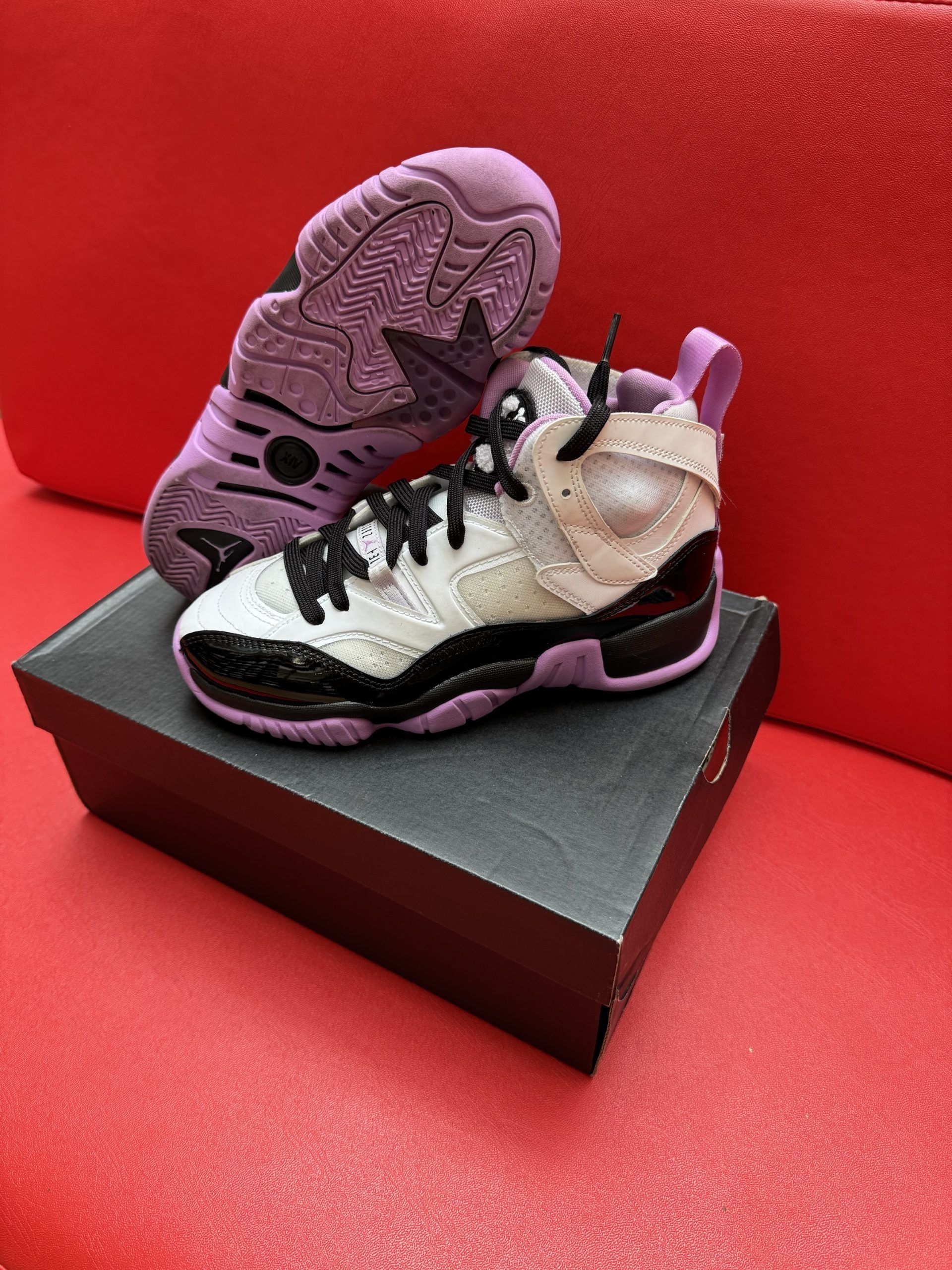 White, black, and purple sneakers on a black box, with a red background.