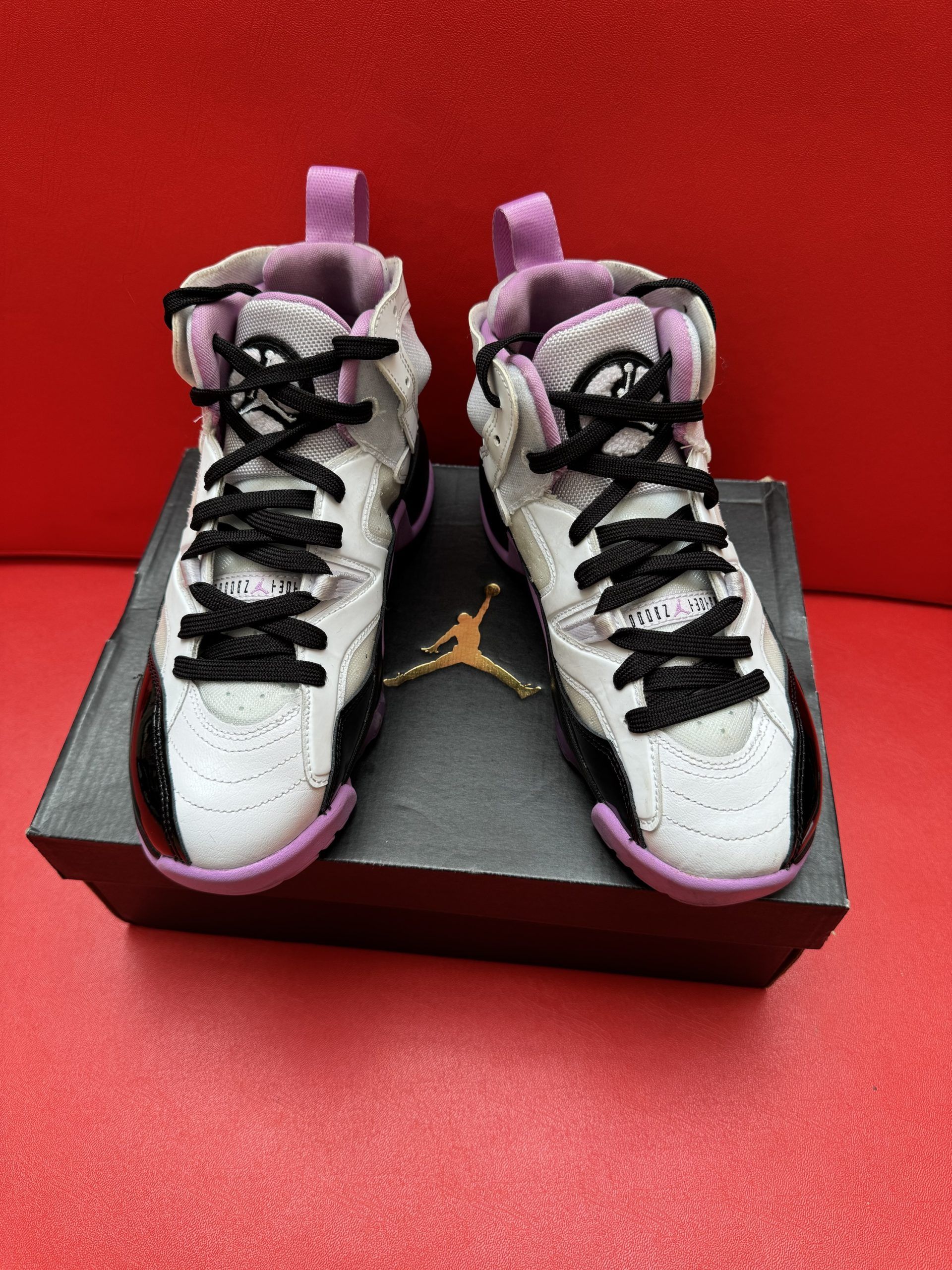 White, black, and purple sneakers on a black box, with a red background.