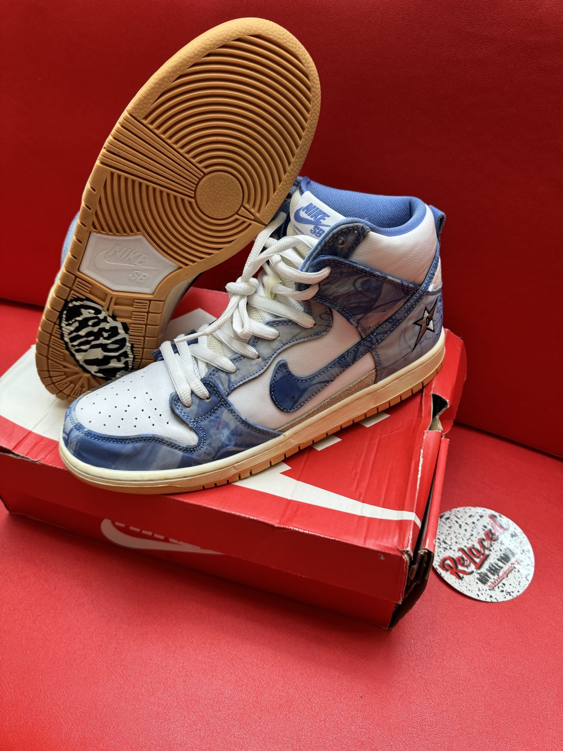 Nike Dunk High sneakers with blue denim-like design, white laces, and gum soles, resting on a red Nike box.