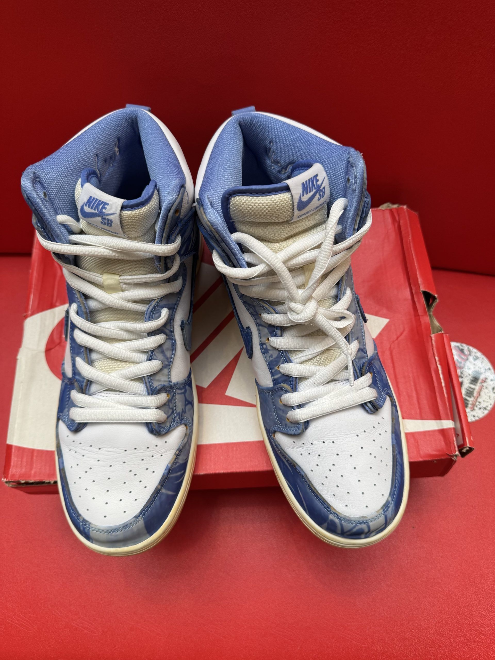 Nike Dunk High sneakers with blue denim-like design, white laces, and gum soles, resting on a red Nike box.