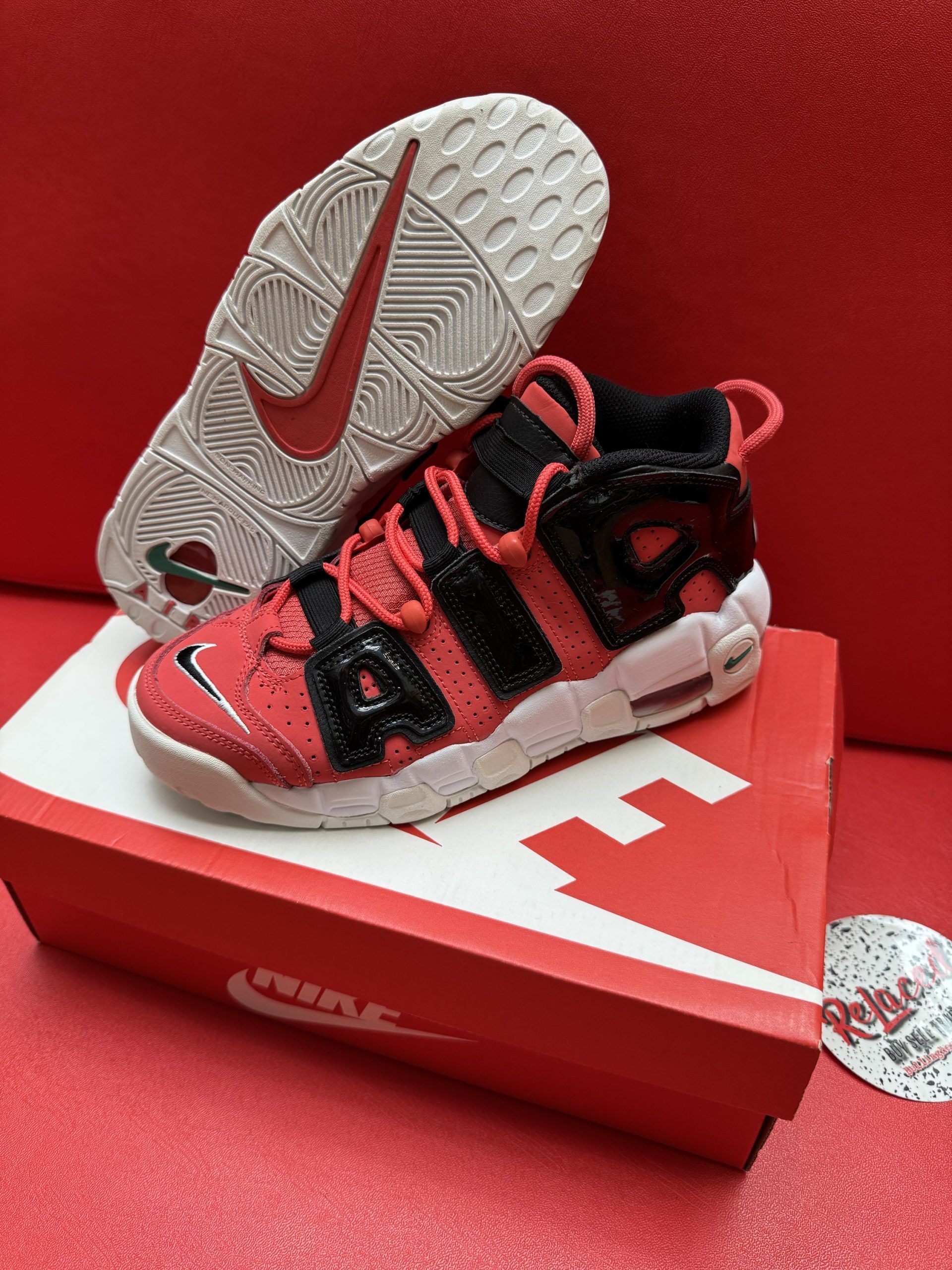 Red and black Nike Air More Uptempo shoe atop a red Nike box, with the sole visible.