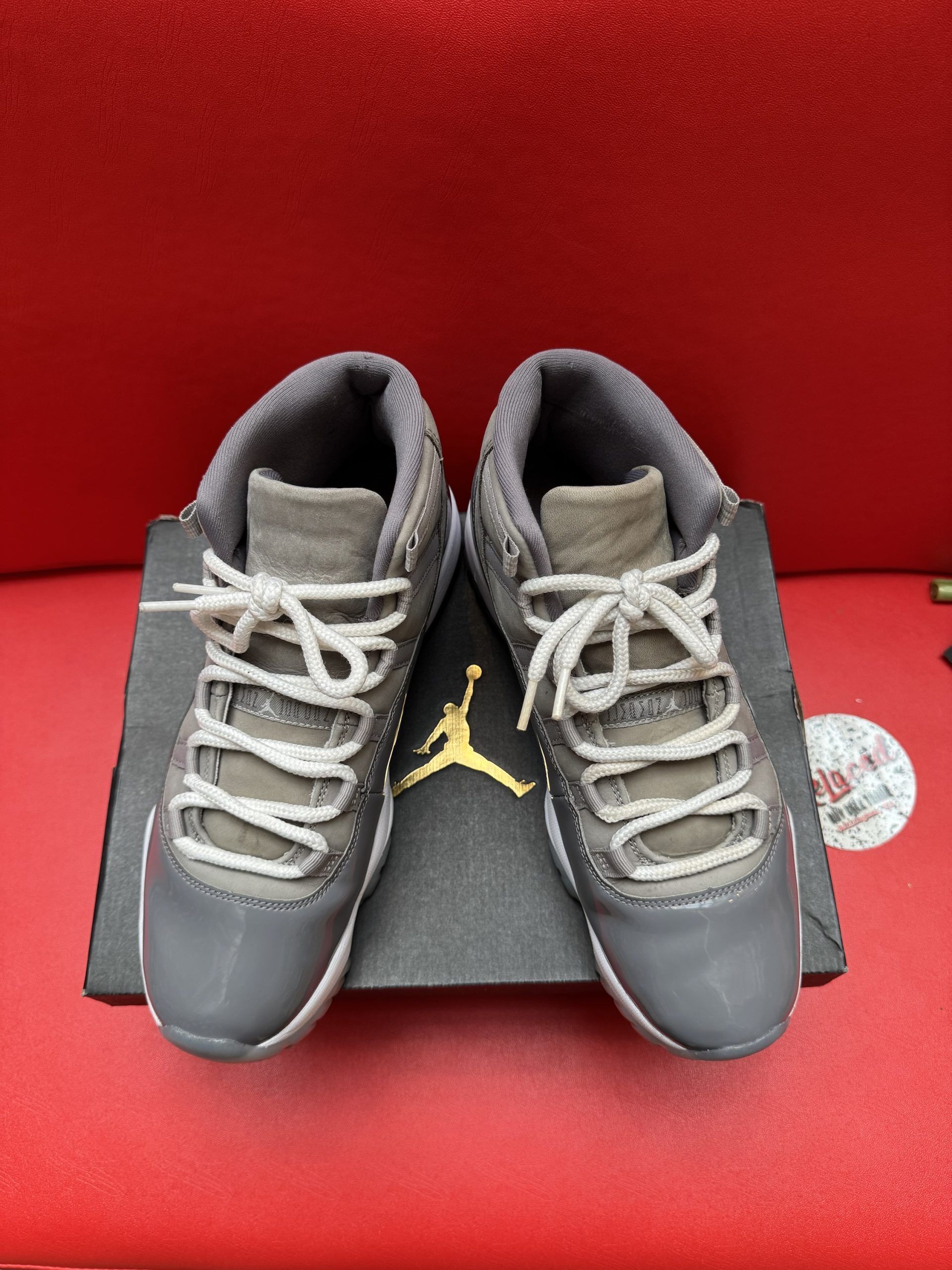 Pair of grey and white Air Jordan 11 Retro sneakers on a black shoebox, red background.