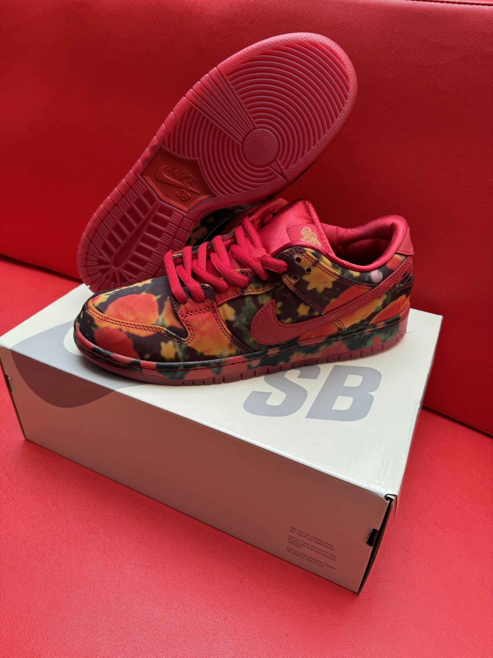 Red and floral Nike SB Dunk Low sneakers on a white box, set against a red background.