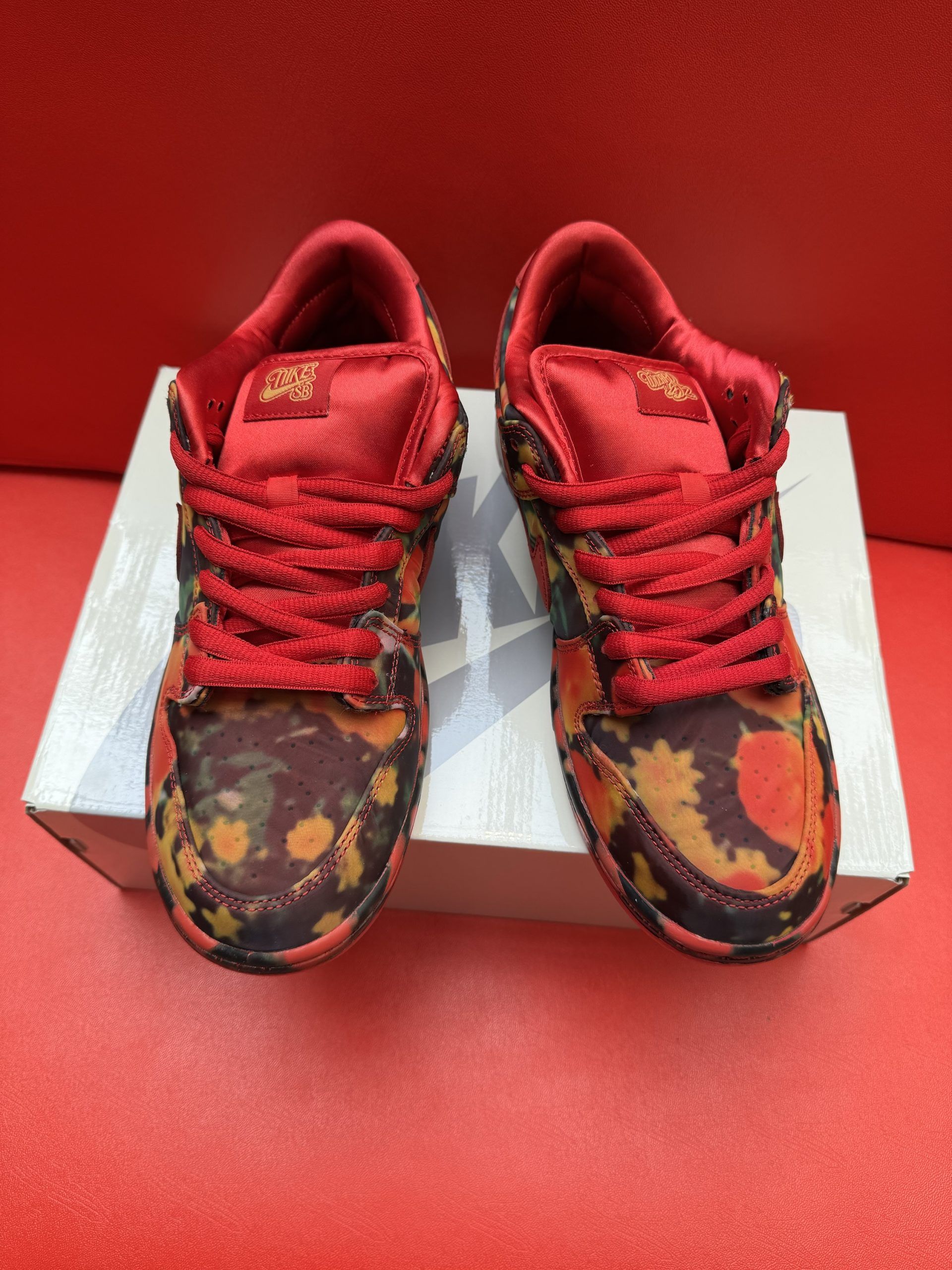 Red and floral Nike SB Dunk Low sneakers on a white box, set against a red background.