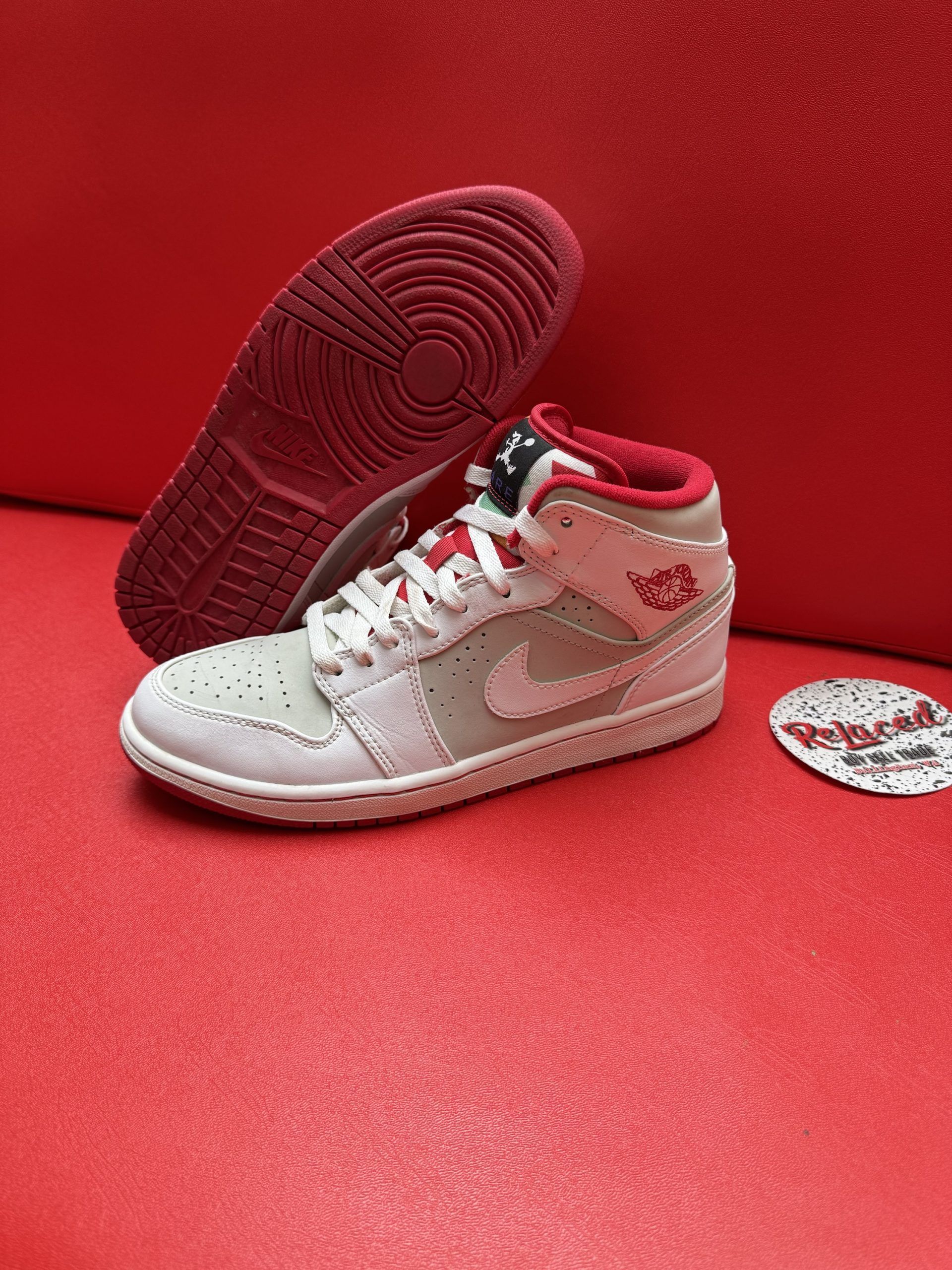 Light grey and white Air Jordan shoe with red accents, sole up, on a red surface.